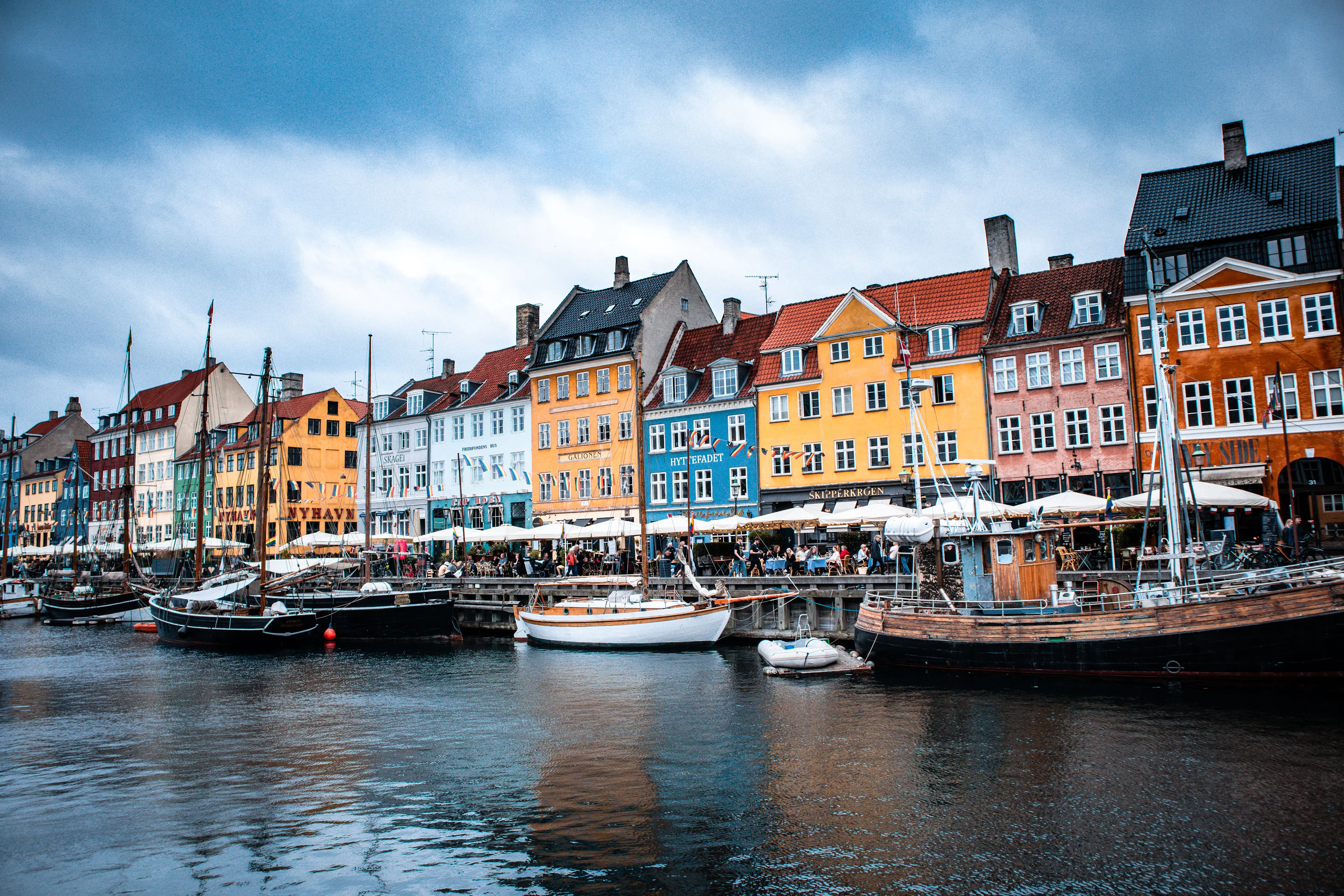 Colourful gabled houses and wooden sailing boats along the Nyhavn canal in Copenhagen under a cloudy blue sky