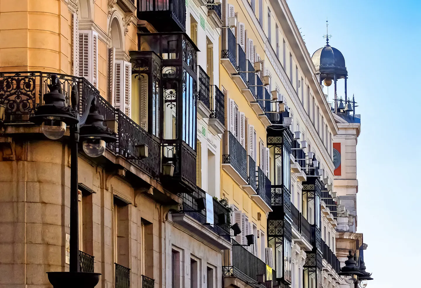 Ornate wrought-iron balconies and glazed miradores along a central Madrid street in warm afternoon light