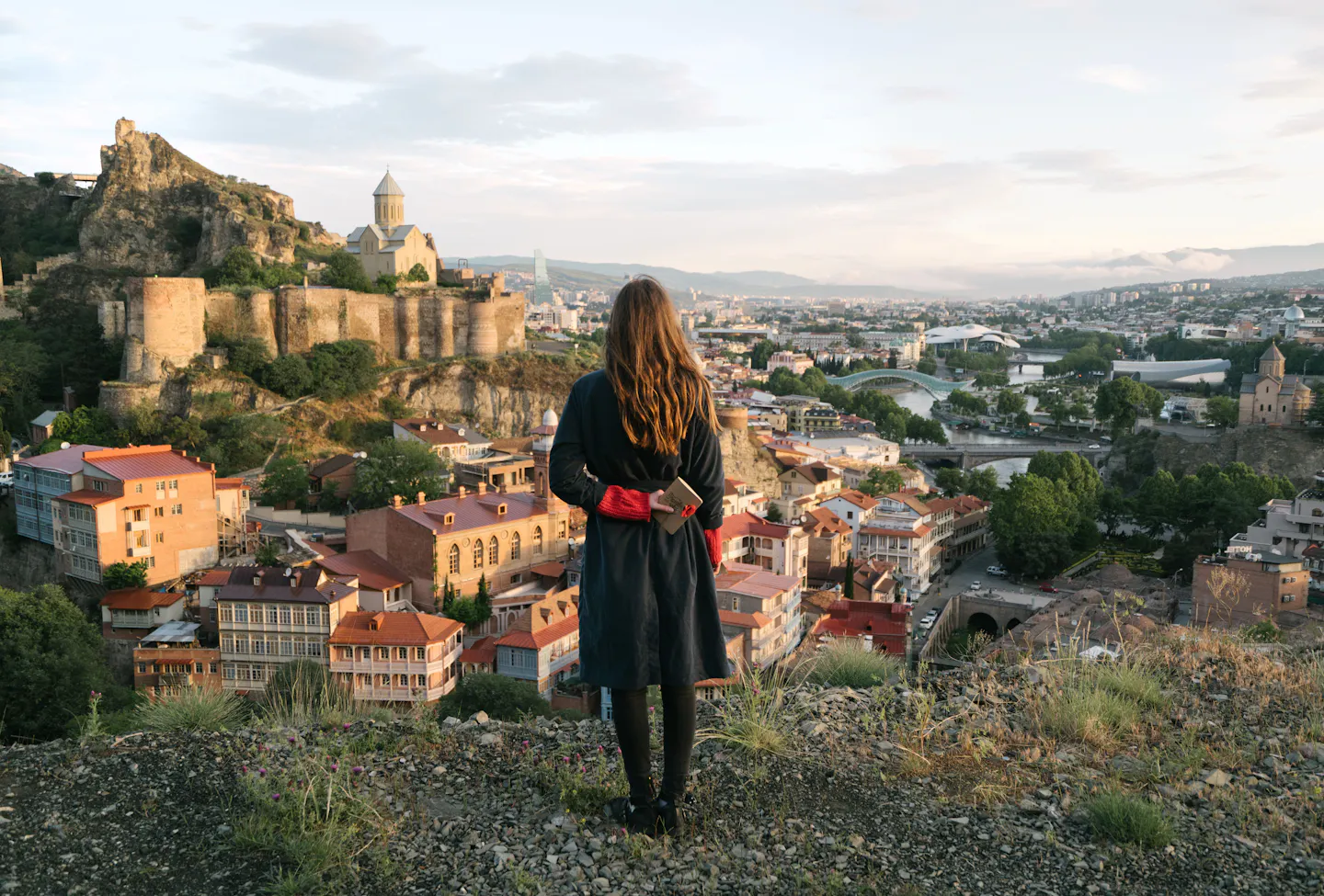 A traveler on a hillside looking out over Tbilisi's Old Town, Narikala Fortress and the Kura River