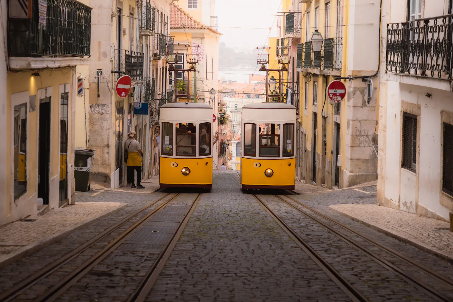 Two yellow Lisbon trams passing each other on a narrow cobbled street between pastel houses