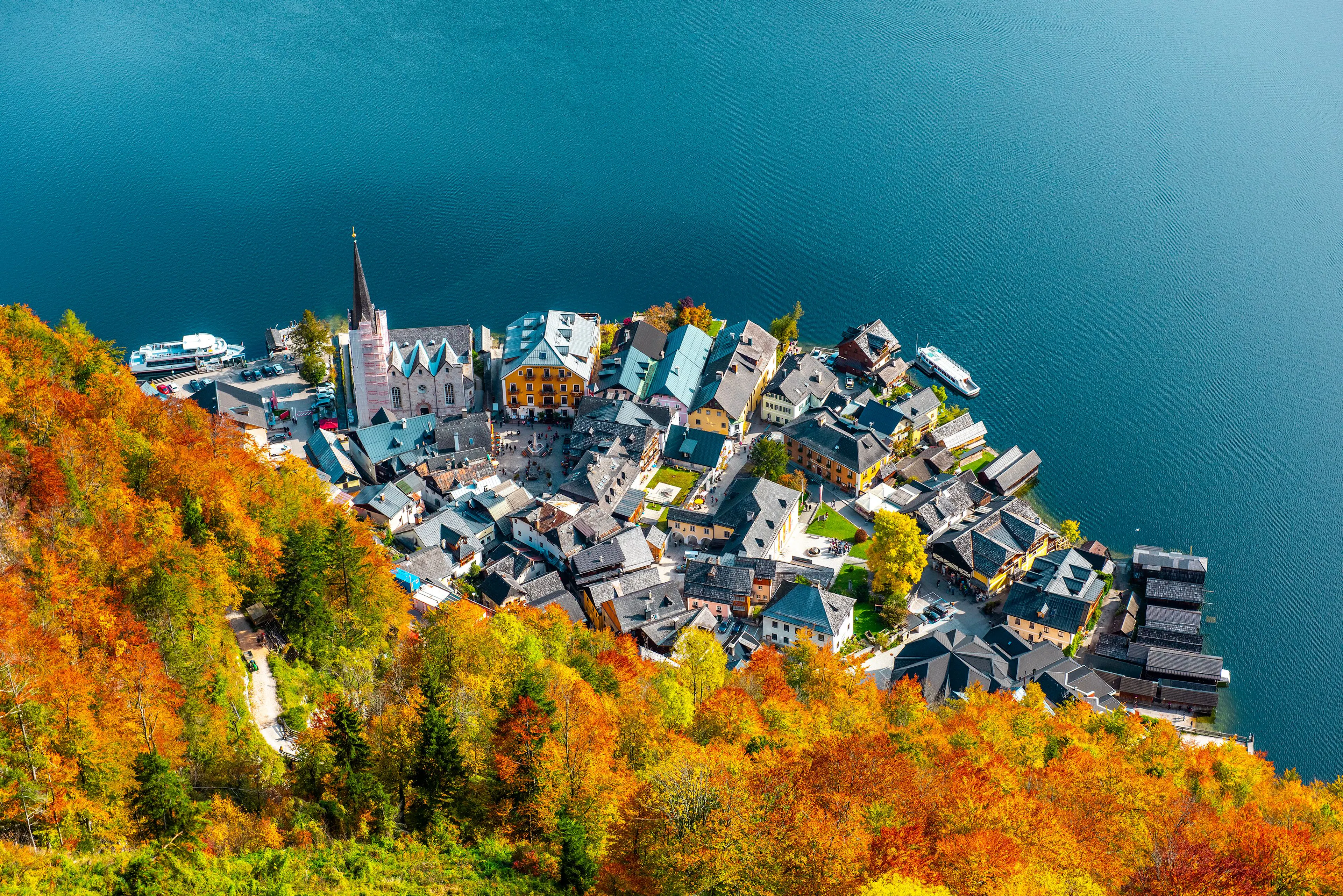 Hallstatt's lakeside village and church seen from above, ringed by forest in bright orange and yellow autumn colour