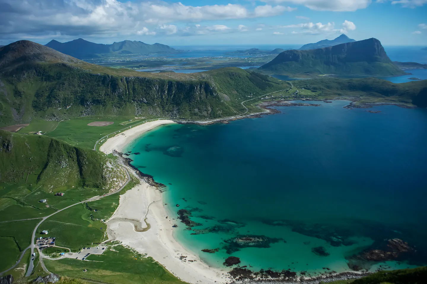 The white sand and turquoise water of Haukland beach below green mountains in Lofoten, Norway