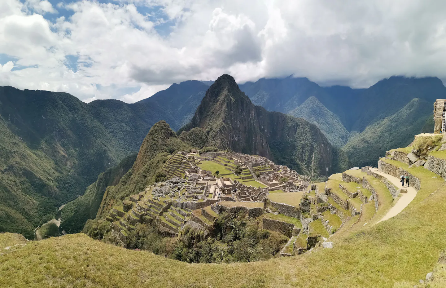 The stone terraces and buildings of Machu Picchu below the peak of Huayna Picchu, green Andean ridges falling away on both sides