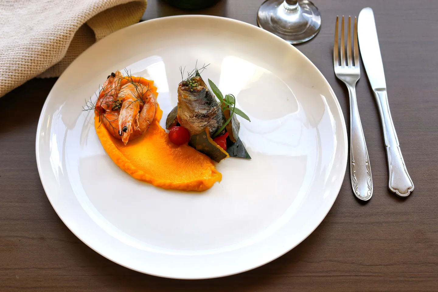 Prawns and rolled sardines beside a smear of orange puree on a white restaurant plate