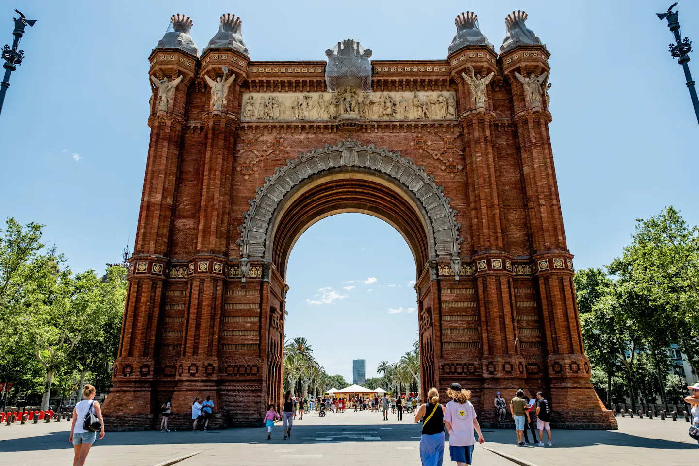 The brick Arc de Triomf in Barcelona seen from below against a clear blue sky, with people walking through the arch