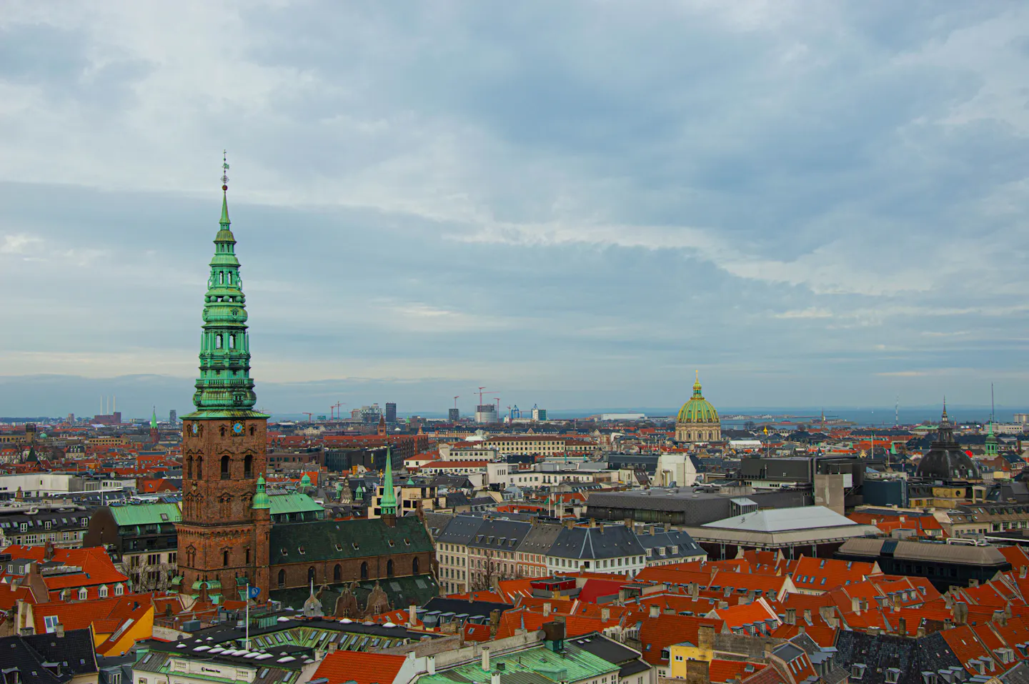 Copenhagen's orange rooftops and the green copper spire of St Nicholas seen from above, with the sea beyond