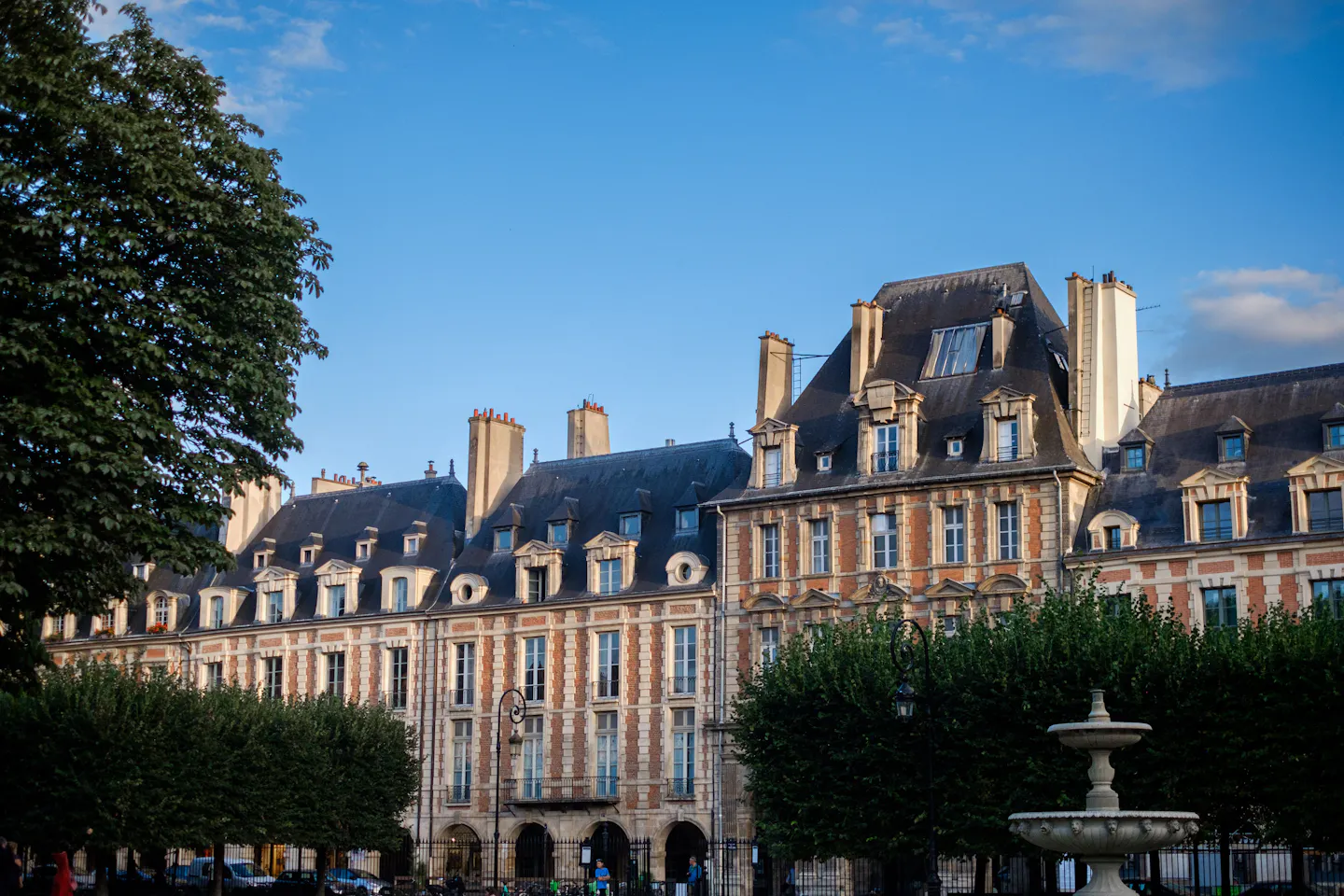 Brick and stone facades with steep mansard roofs around Place des Vosges in warm evening light