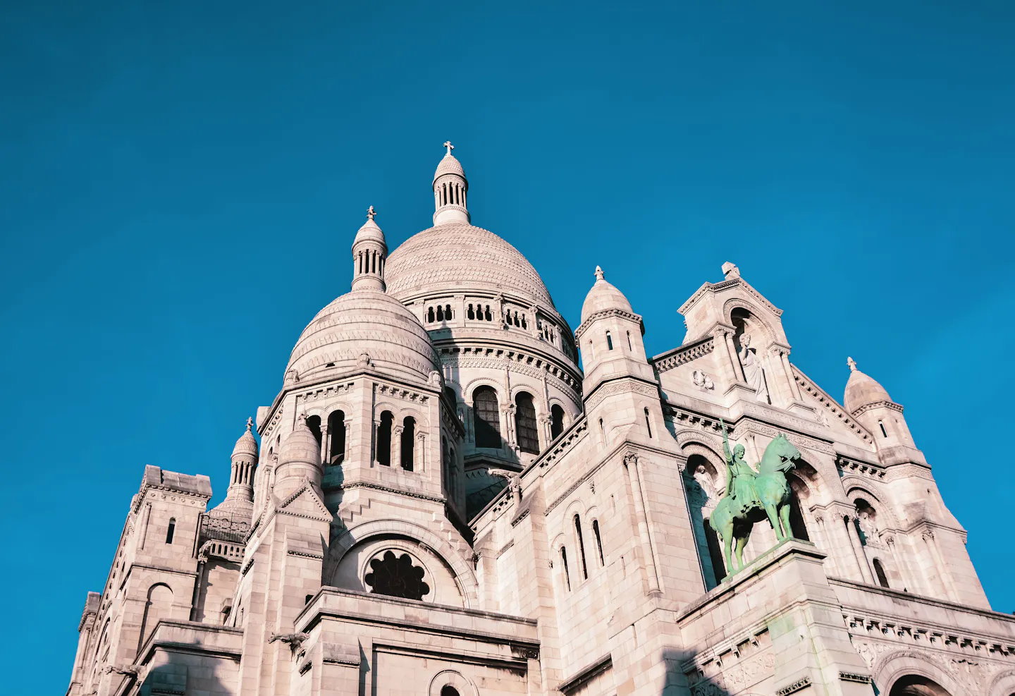 The white domes and turrets of the Sacre-Coeur basilica in Montmartre against a deep blue sky