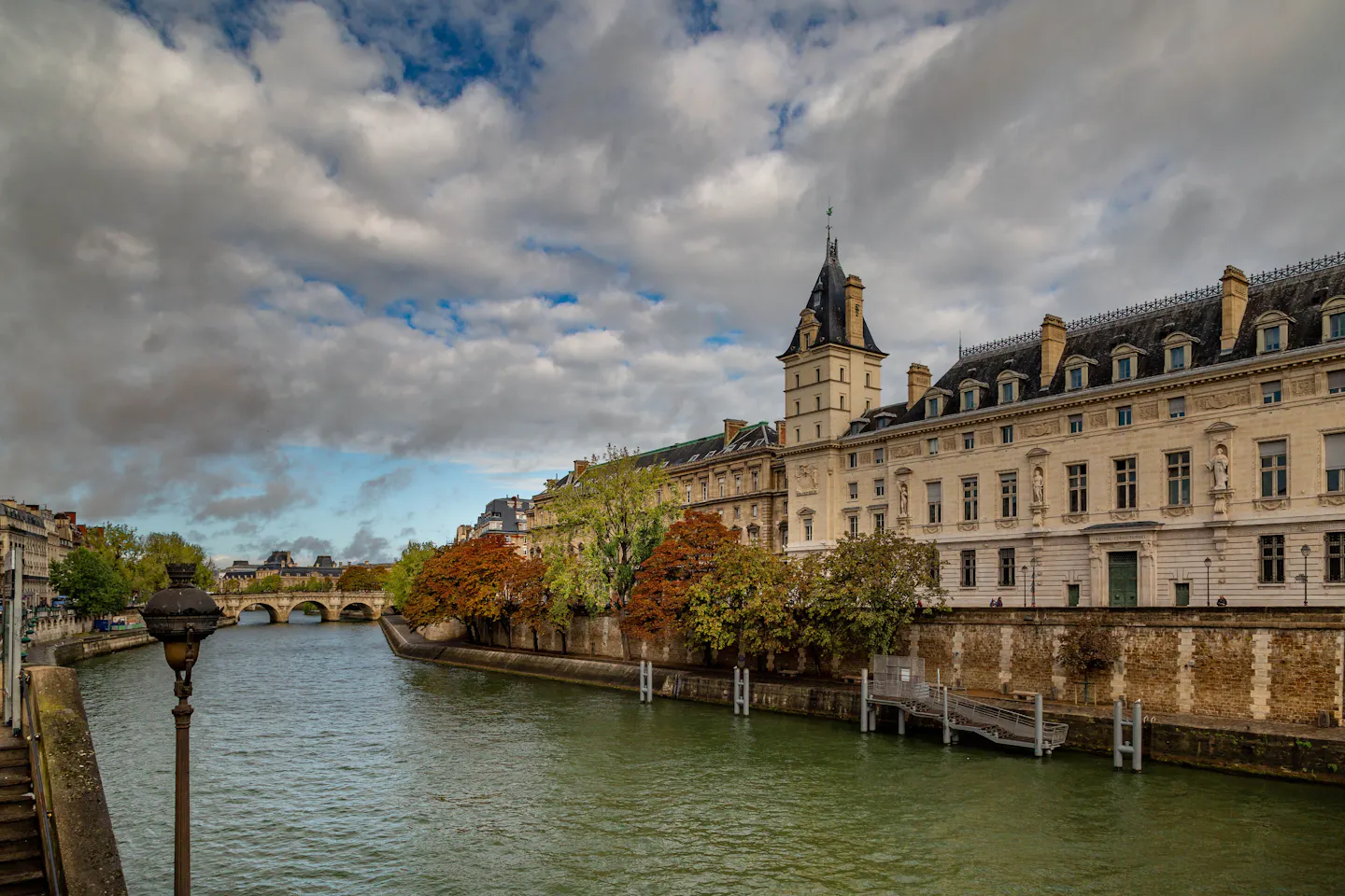 Stone quay buildings and autumn trees along the Seine in central Paris under a dramatic cloudy sky