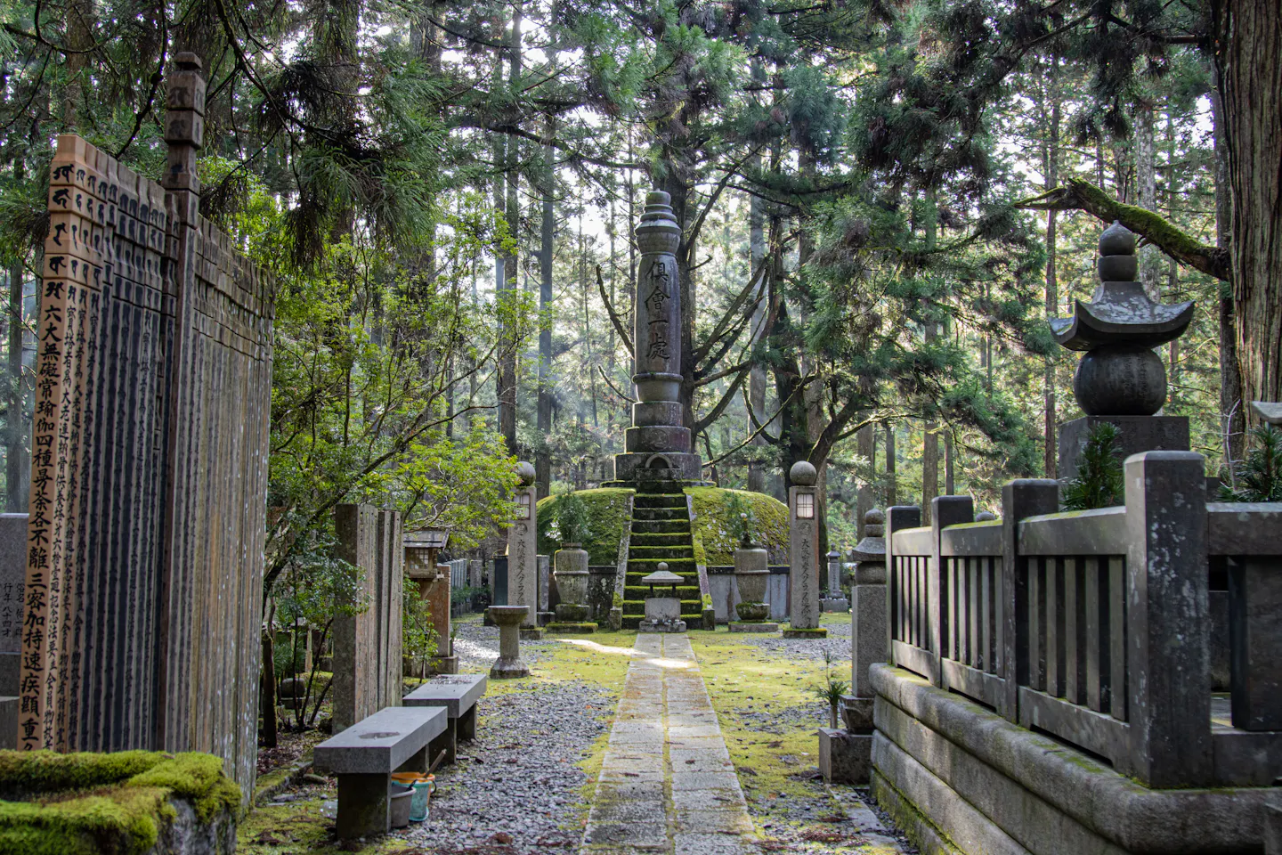 Moss-covered stone monuments and a path between tall cedars at Okunoin cemetery in Koyasan