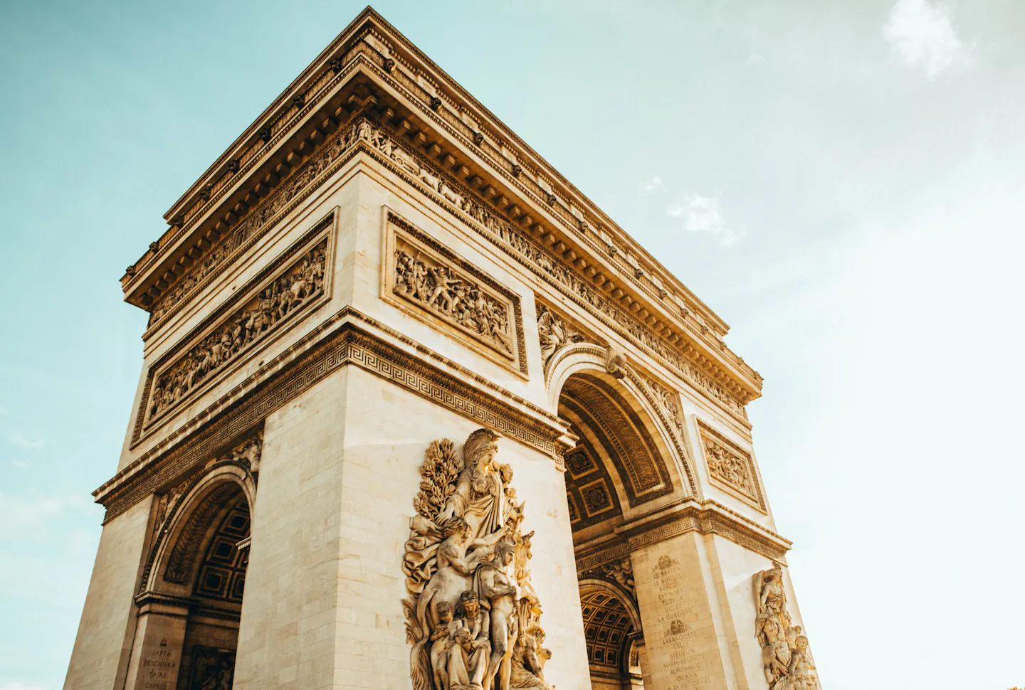 The sculpted stone facade of the Arc de Triomphe seen from below in warm light