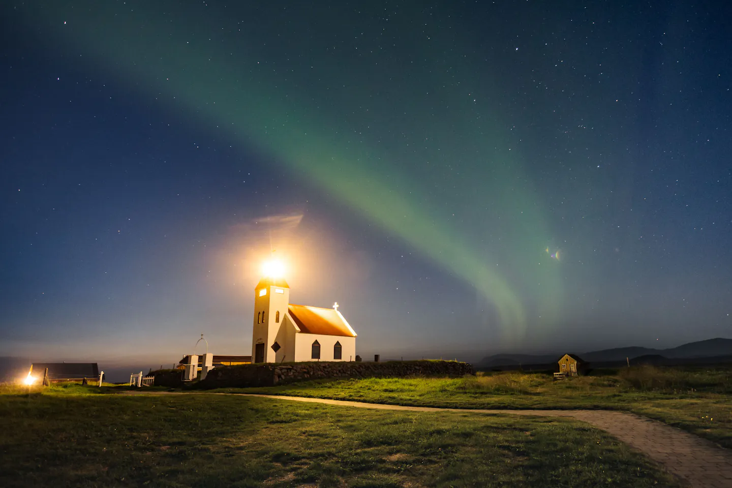 A small lit church under a faint green aurora over open grass on a clear autumn night in Iceland