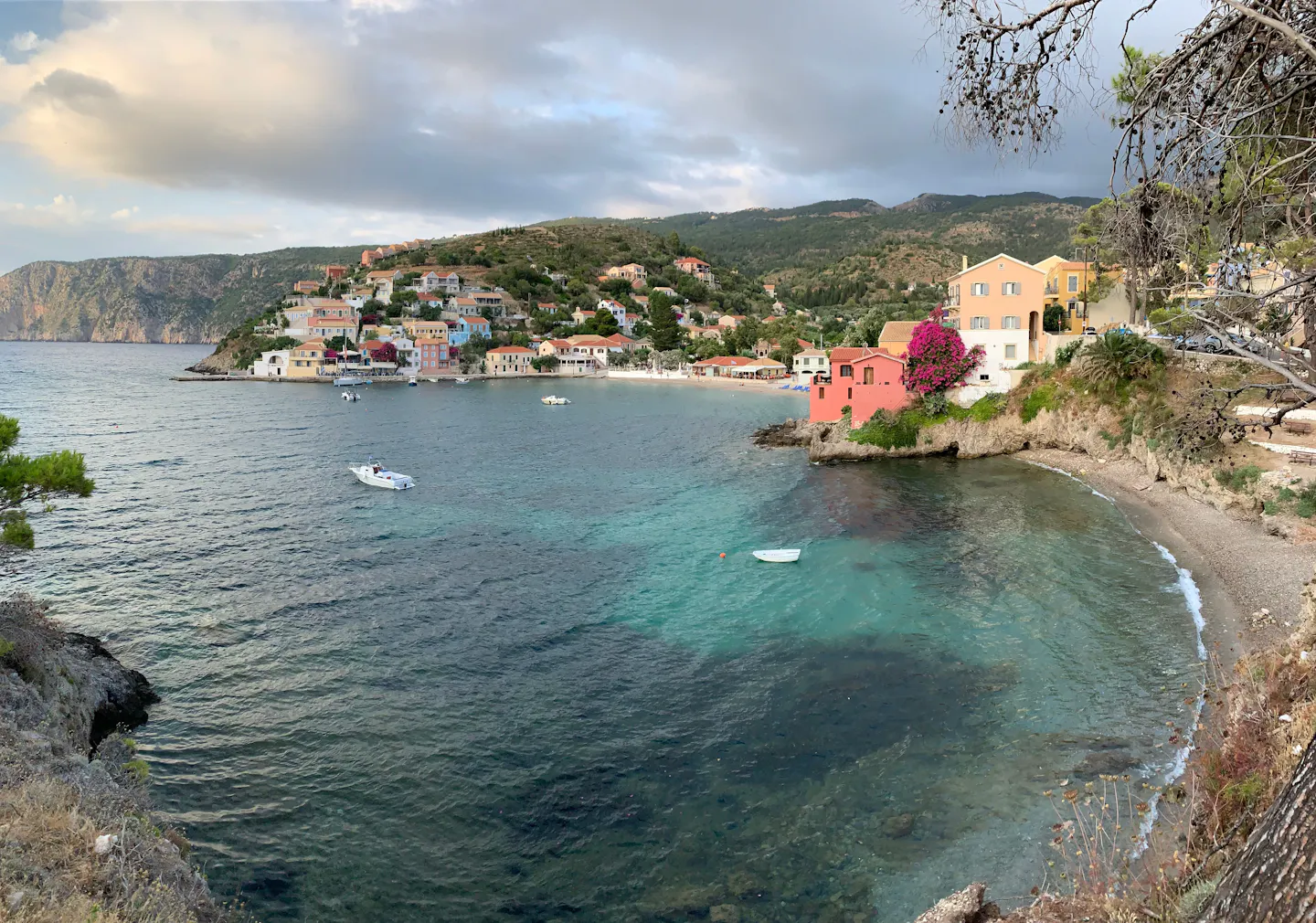 Pastel-coloured houses of Assos wrapped around a clear turquoise bay on Kefalonia, framed by pine branches