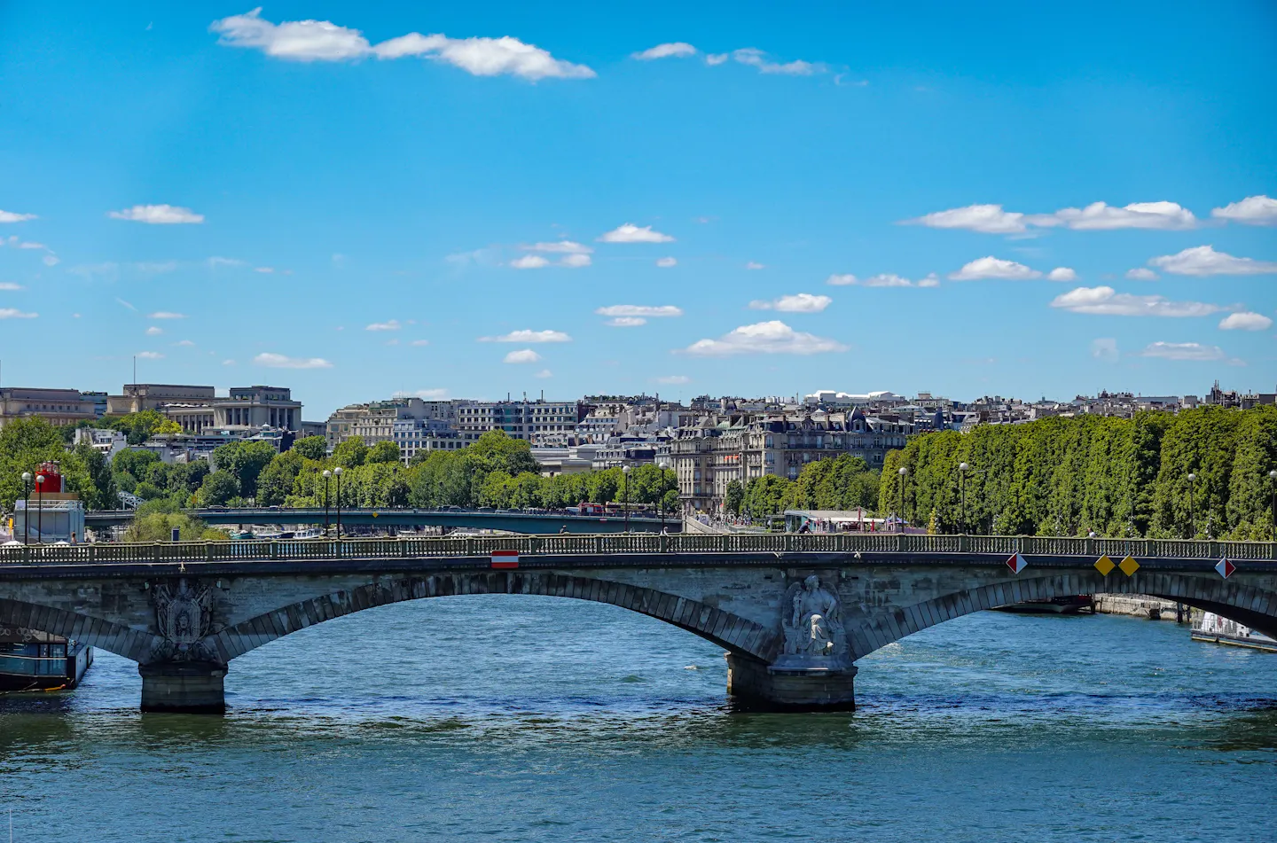 A stone bridge with sculpted piers spanning the Seine under a bright blue sky in central Paris