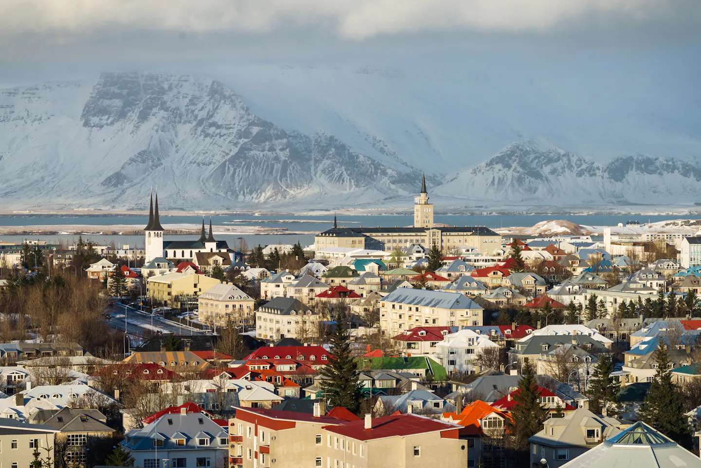 A panoramic winter view of Reykjavík, Iceland, with colorful rooftops, churches, and snow-covered mountains.