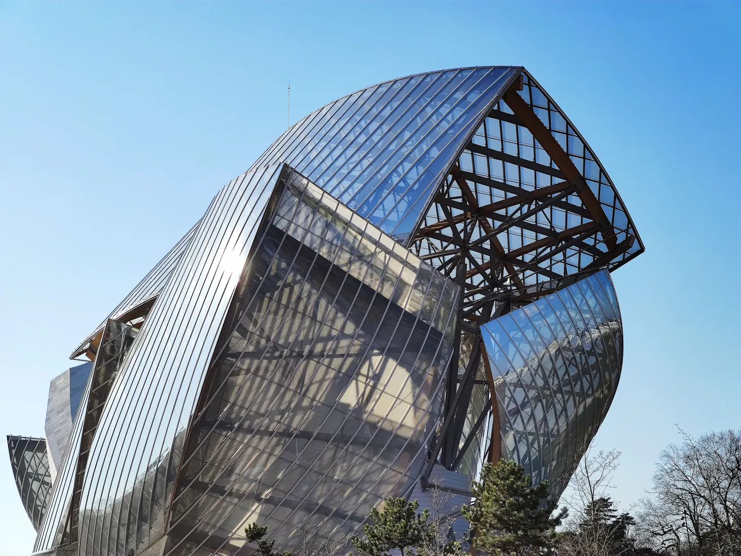 The curved glass sails and timber frame of the Fondation Louis Vuitton against a clear blue sky
