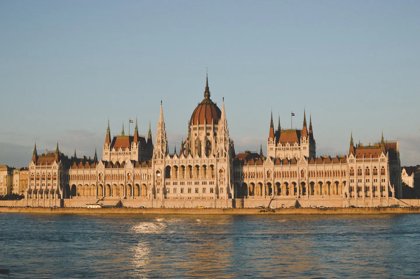 The Hungarian Parliament along the Danube in Budapest, its long facade lit warm at sunset