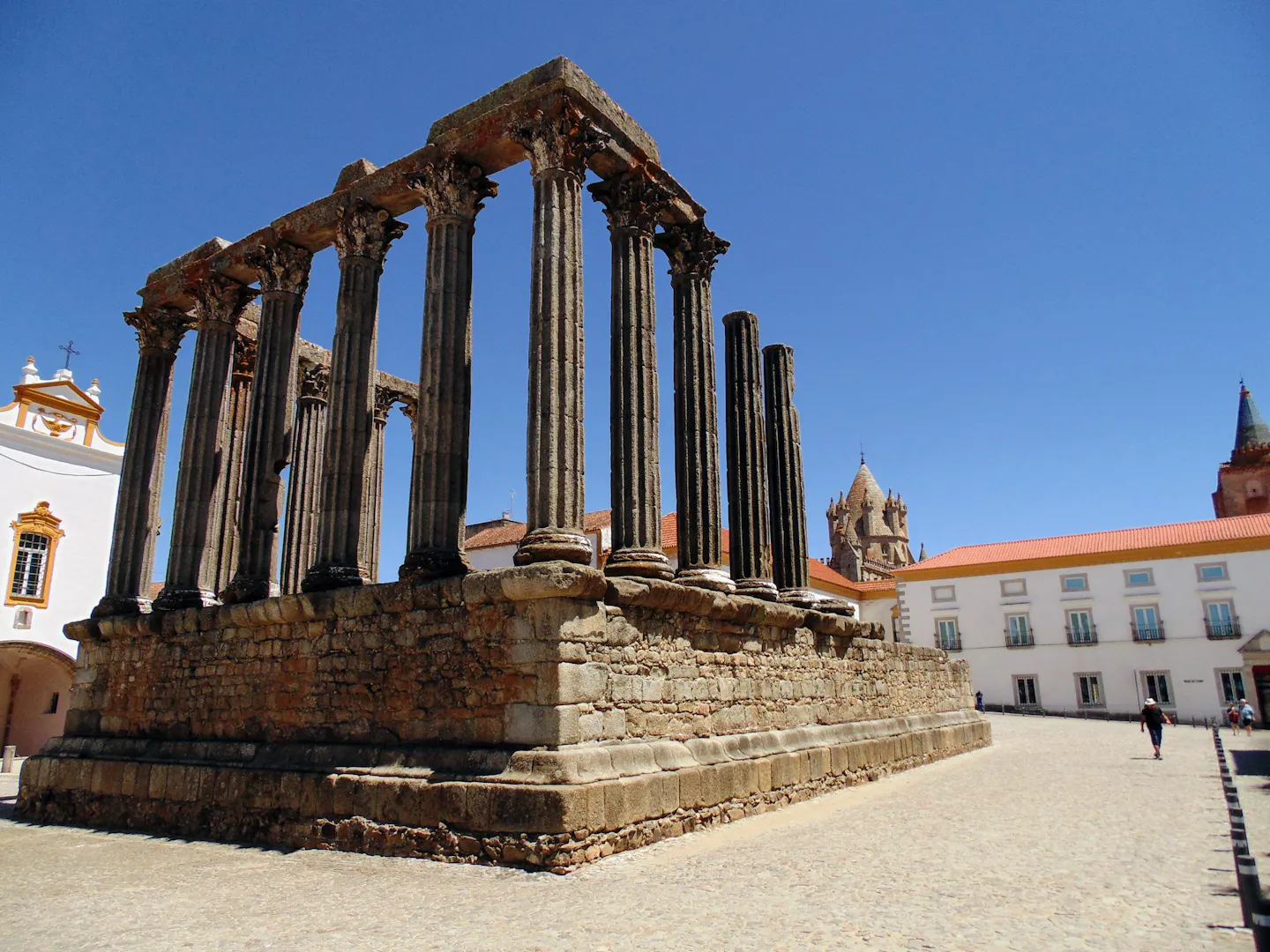 Roman temple columns on a cobbled square in Évora, Portugal, with whitewashed buildings under a deep blue sky