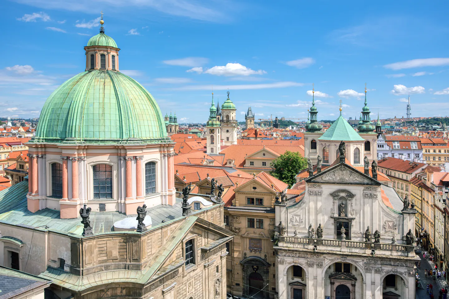 Baroque domes, spires and terracotta rooftops of Prague's Old Town under a bright blue sky