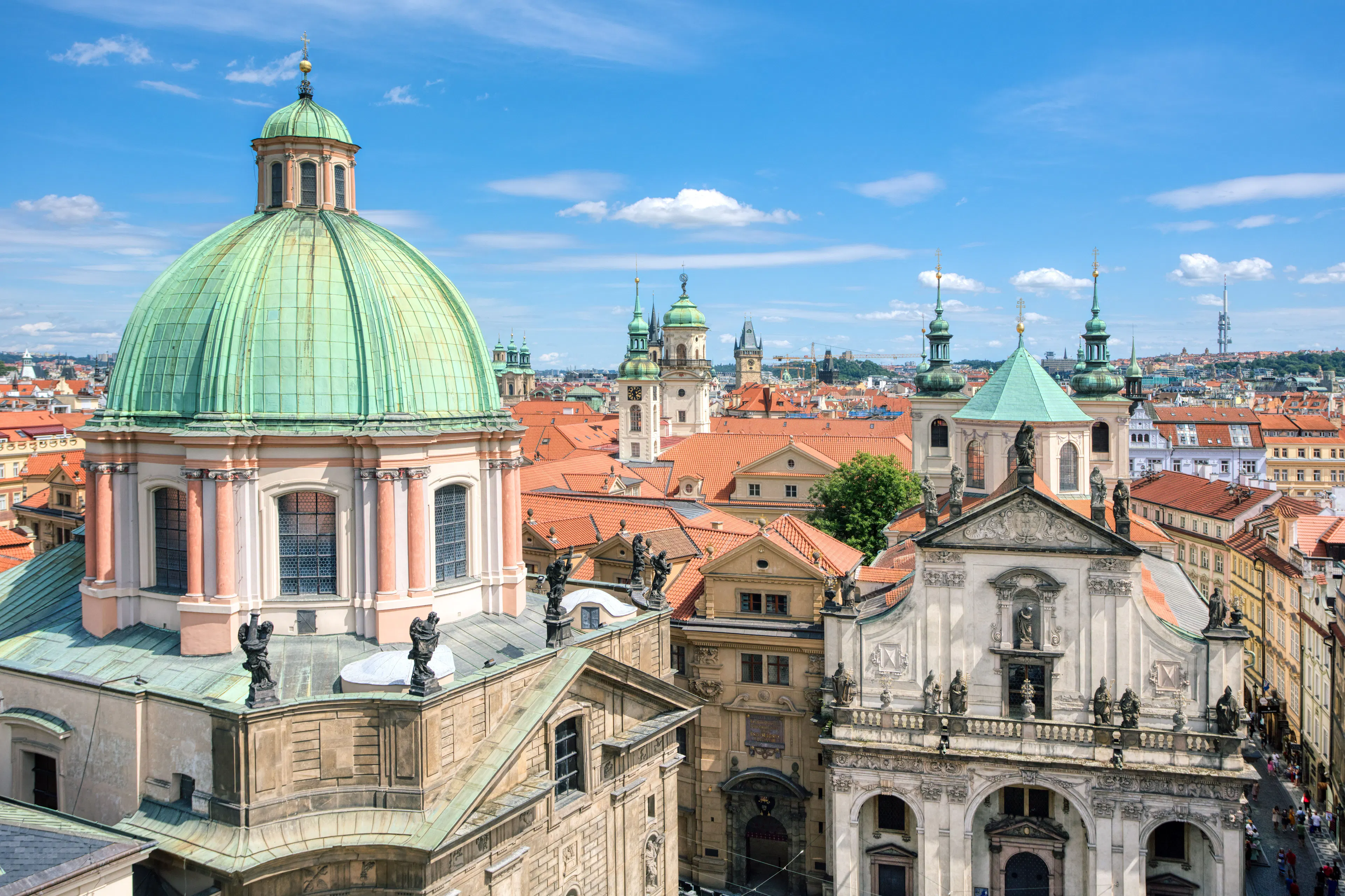Baroque domes, spires and terracotta rooftops of Prague's Old Town under a bright blue sky