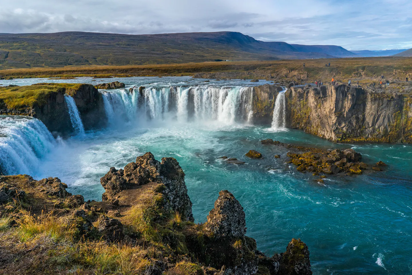 The wide curving falls of Goðafoss pouring into bright turquoise water below open Icelandic moorland