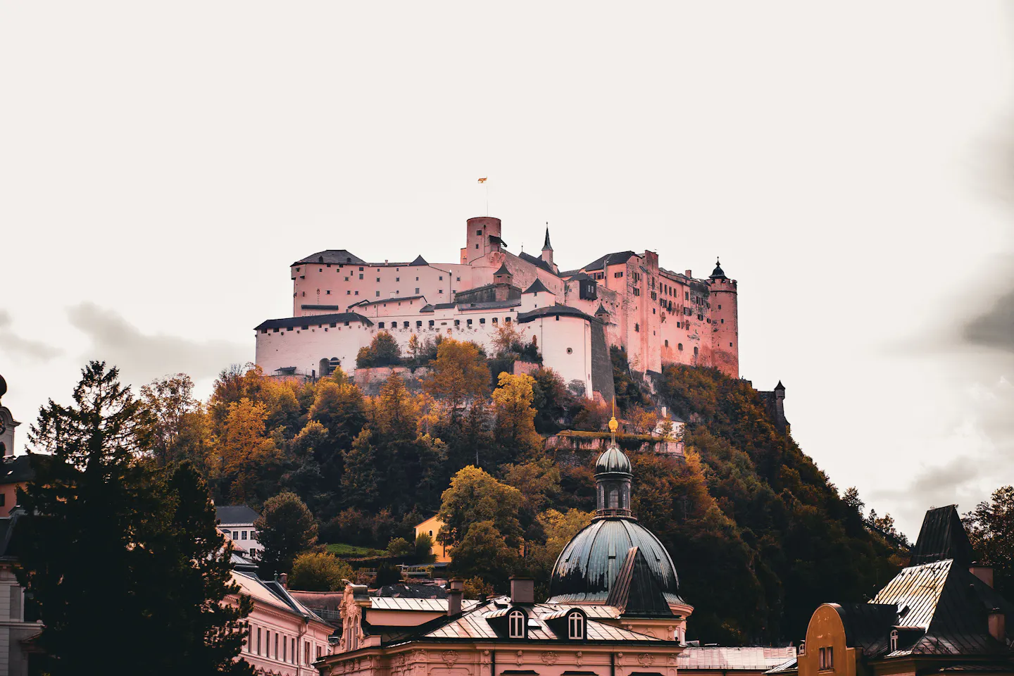 Hohensalzburg Fortress glowing above autumn trees and the domes of Salzburg's Old Town