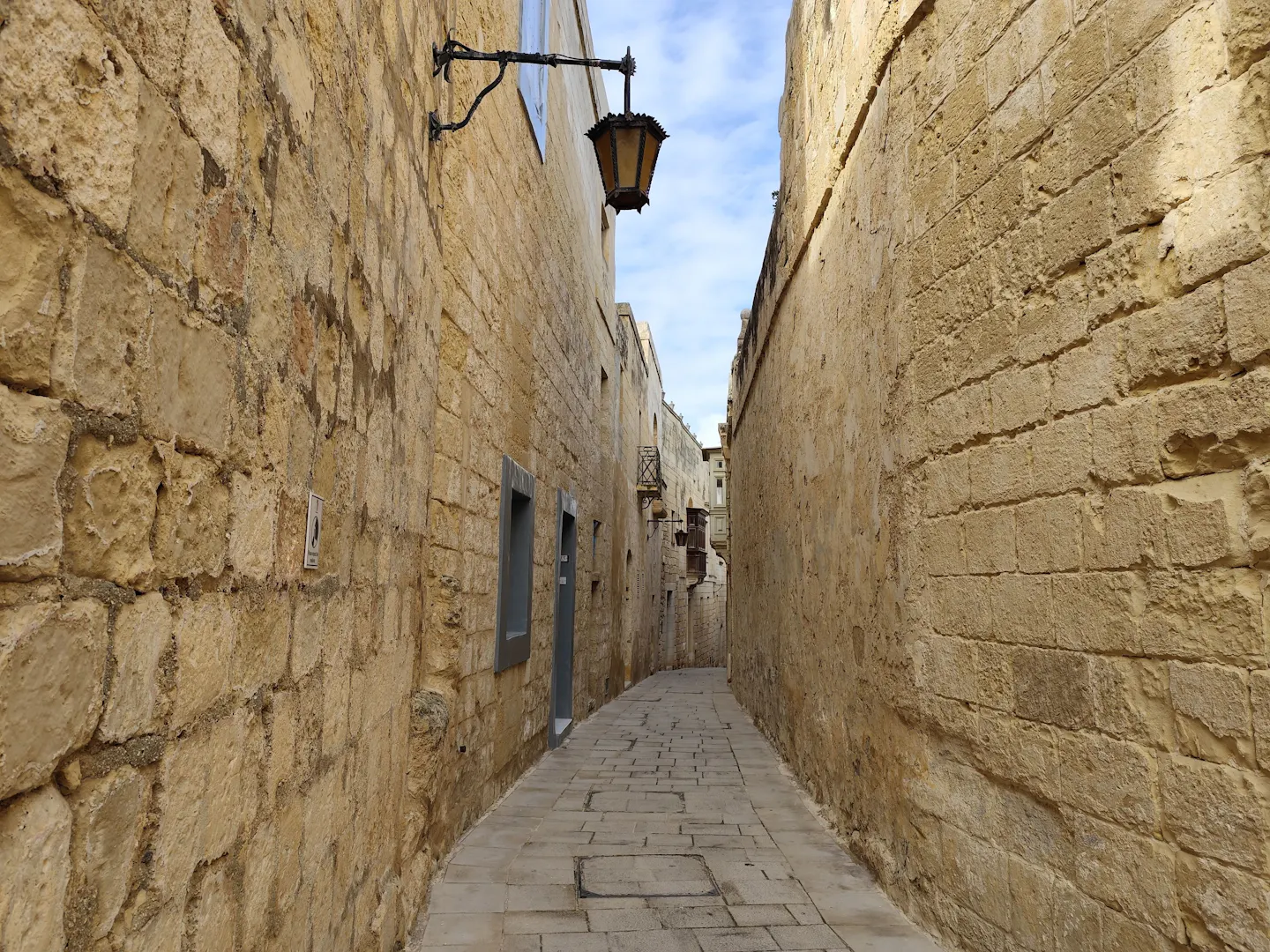 A narrow limestone alley in the walled city of Mdina, Malta, under a strip of blue sky