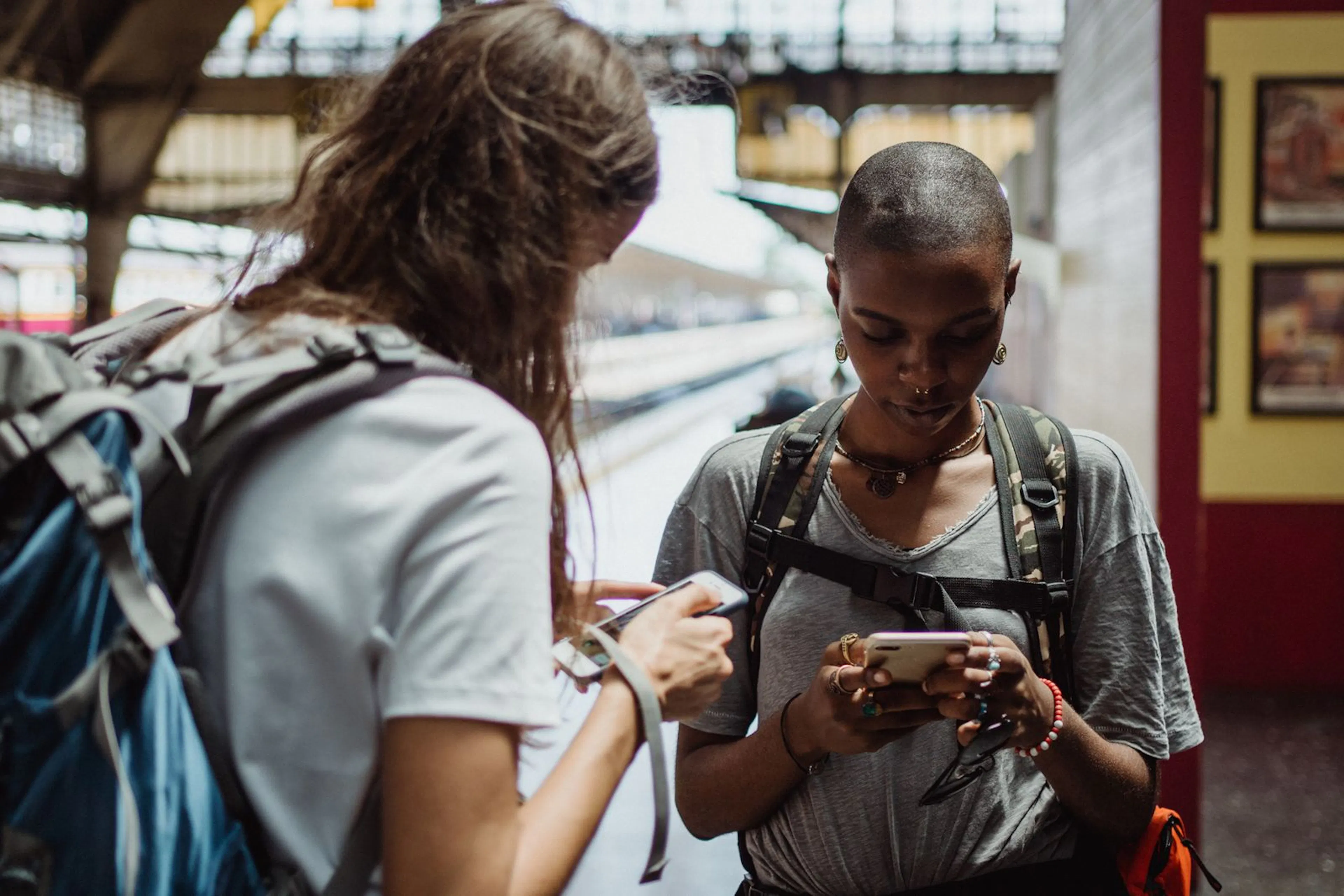 Two travellers checking their phones on a station platform