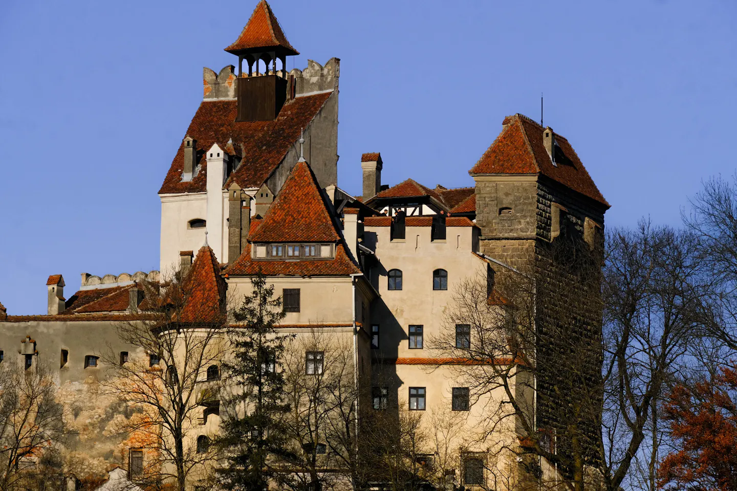 Bran Castle in Transylvania, its red-tiled roofs and stone tower lit by low sun above bare autumn trees