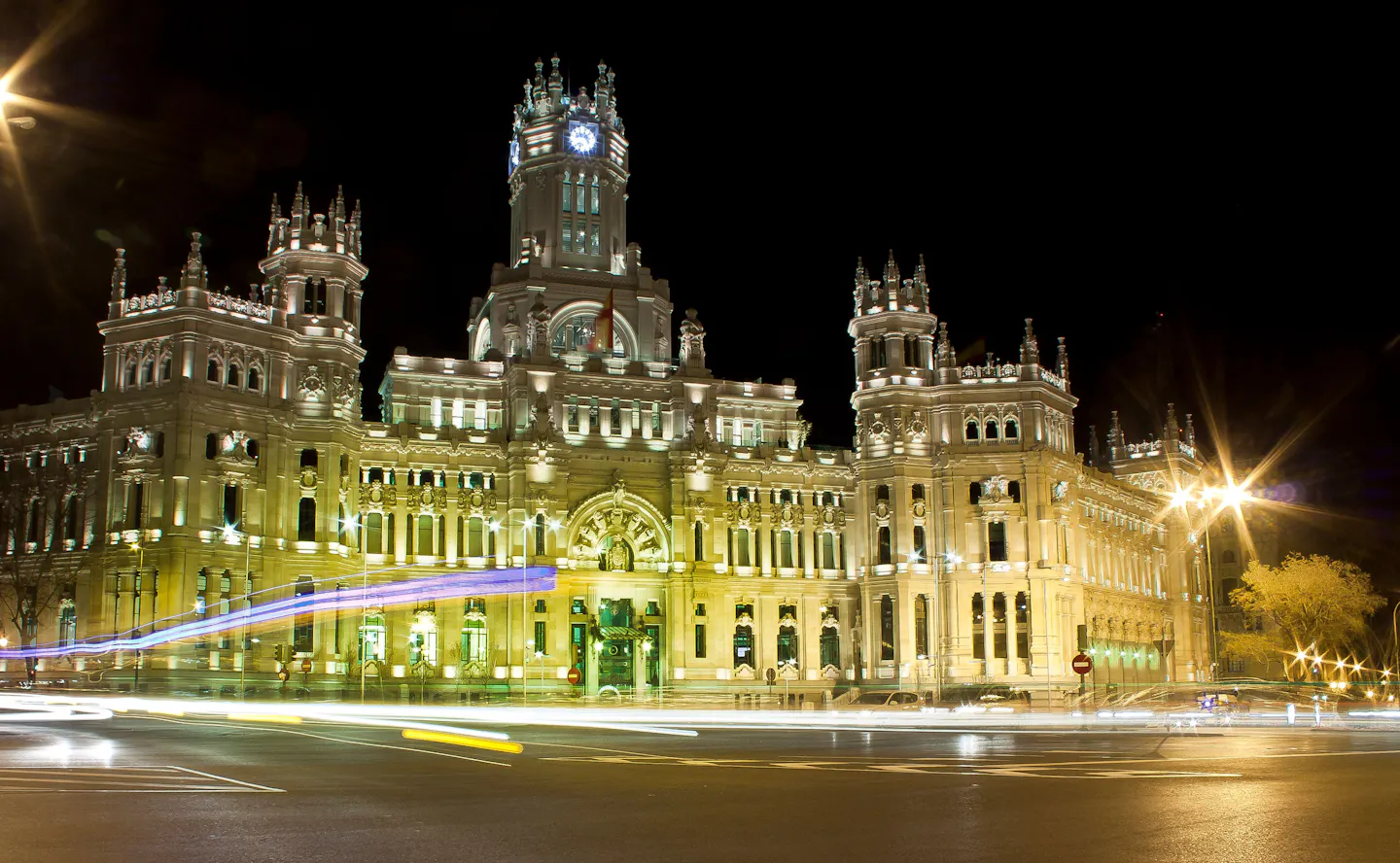 The floodlit Palacio de Cibeles in Madrid at night with car light trails sweeping across the road