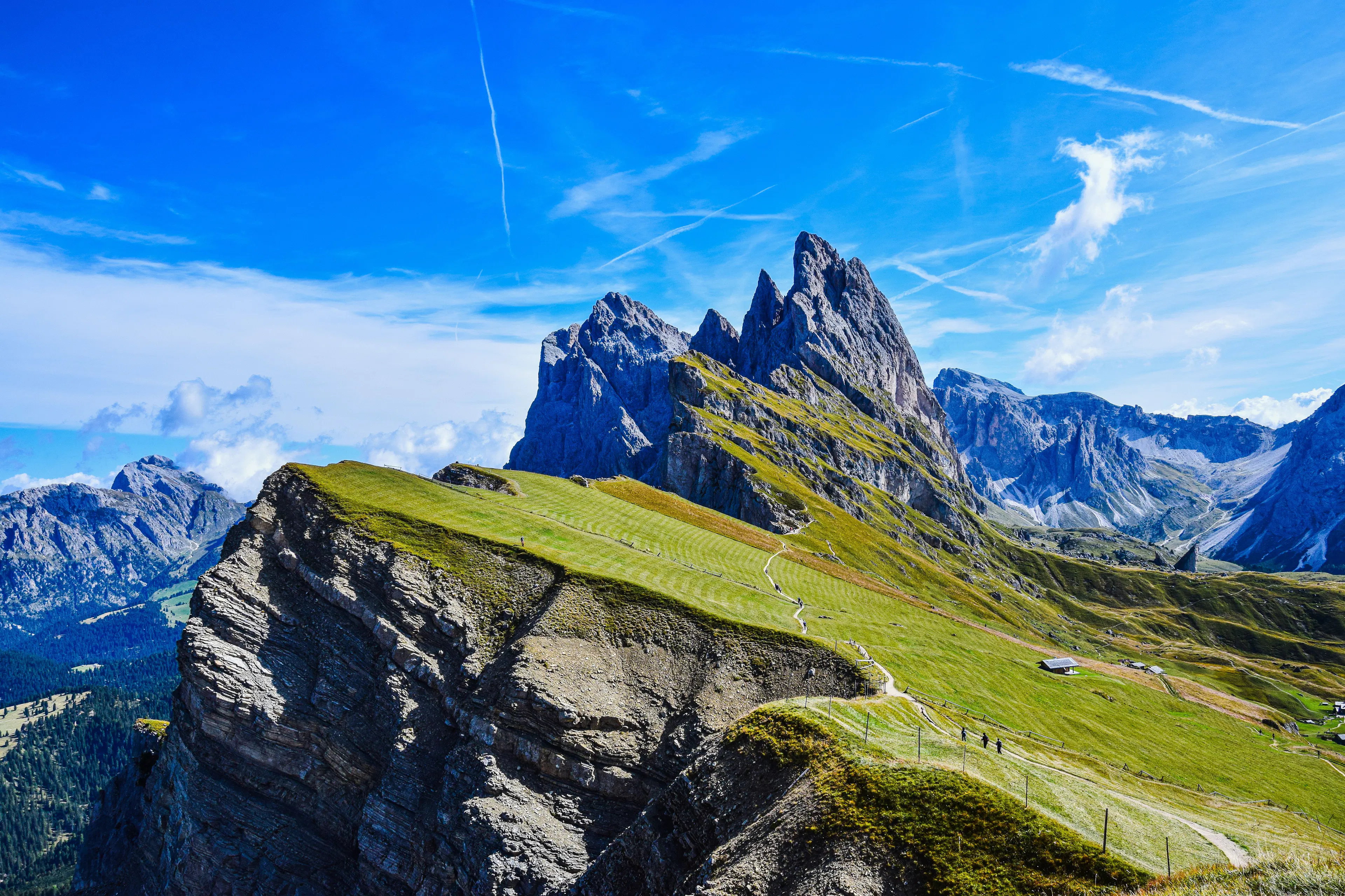 Aerial view of the jagged Dolomite peaks rising above green alpine meadows under a clear blue sky