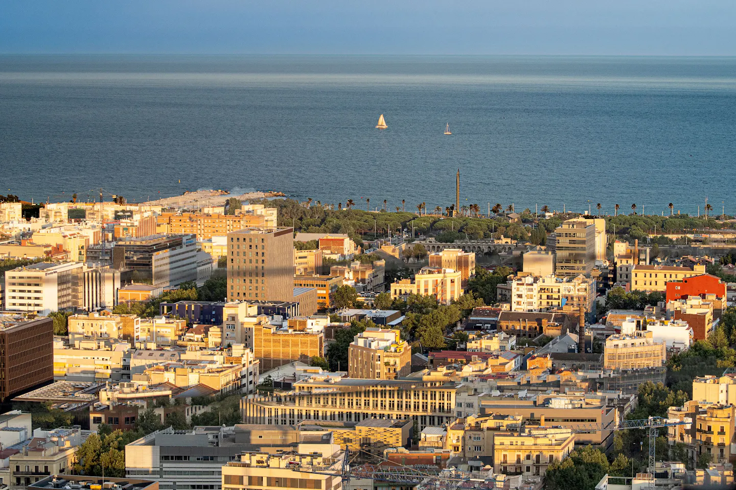 Barcelona rooftops running down to the Mediterranean at golden hour, with two sailboats offshore