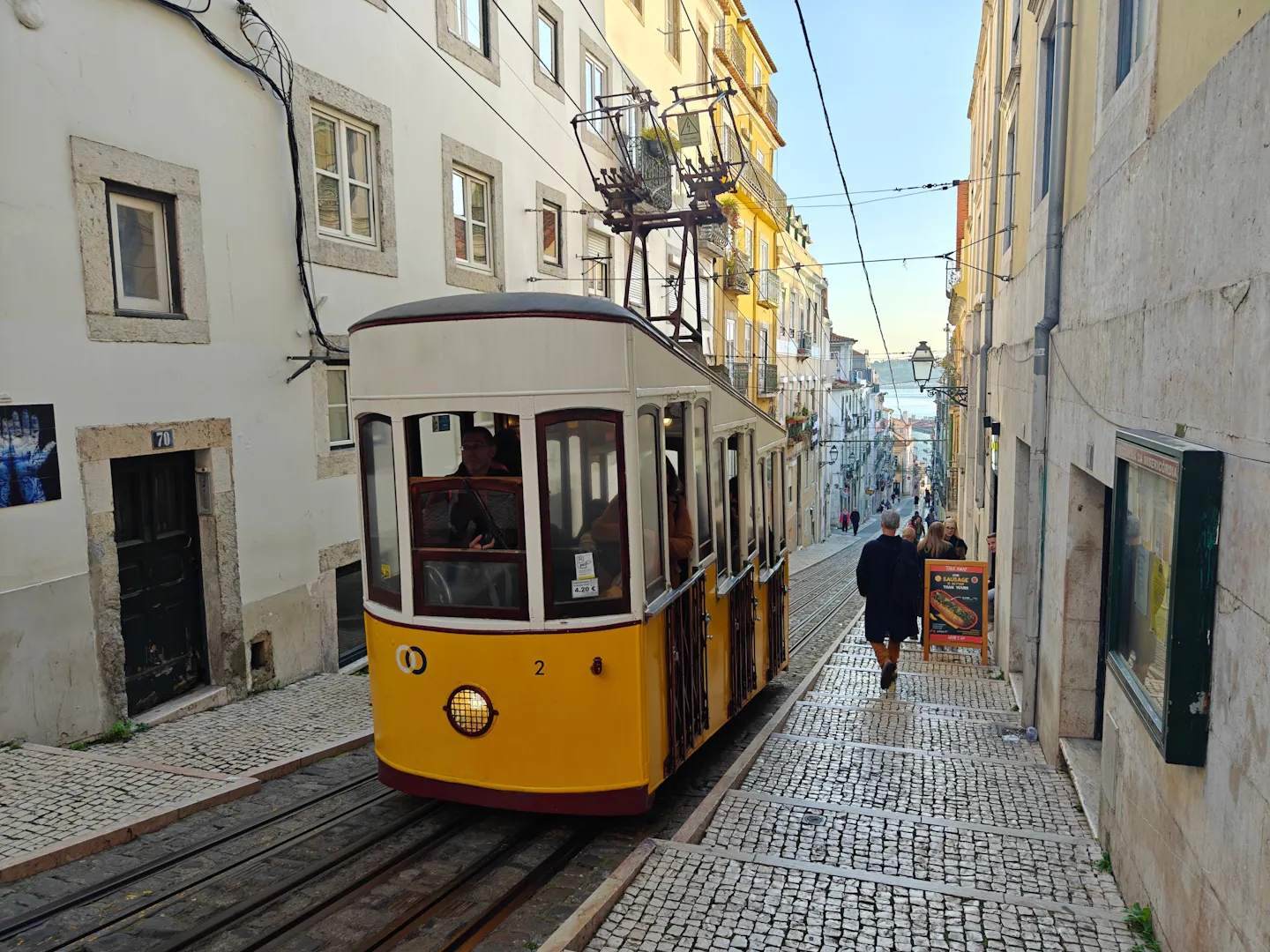A yellow Lisbon tram climbing a narrow cobbled street between pale buildings
