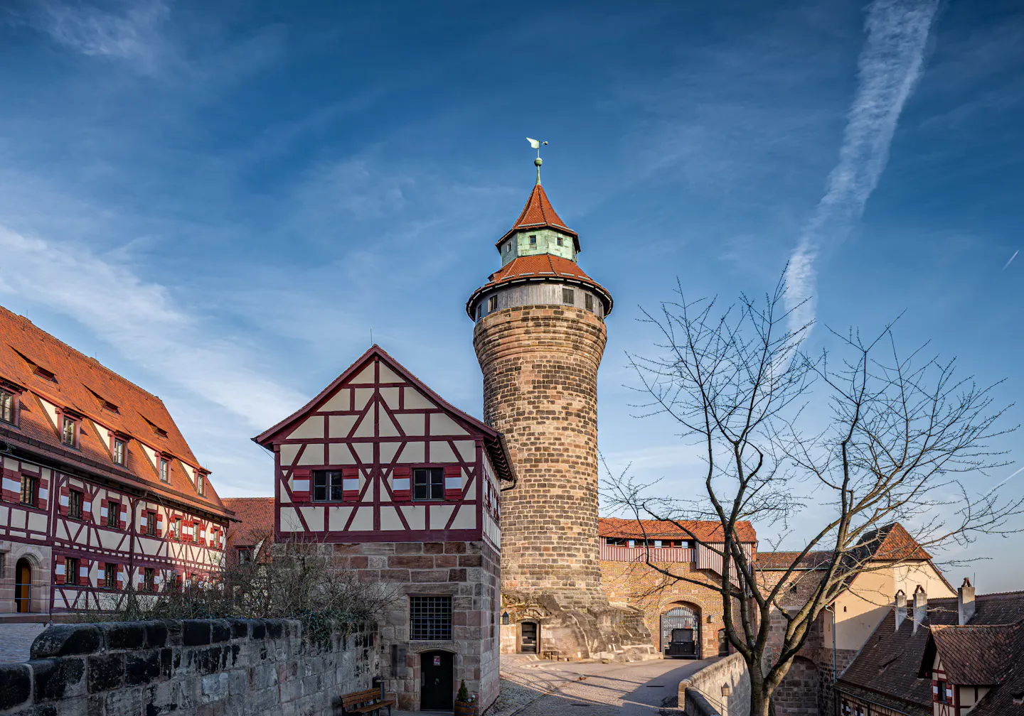 The round Sinwell tower and half-timbered buildings of Nuremberg Castle against a blue sky