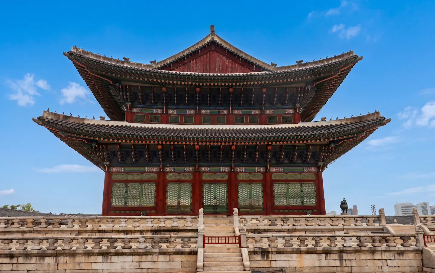 The main throne hall of Gyeongbokgung Palace in Seoul, its double tiled roof and red, green and gold painted timberwork against a bright blue sky