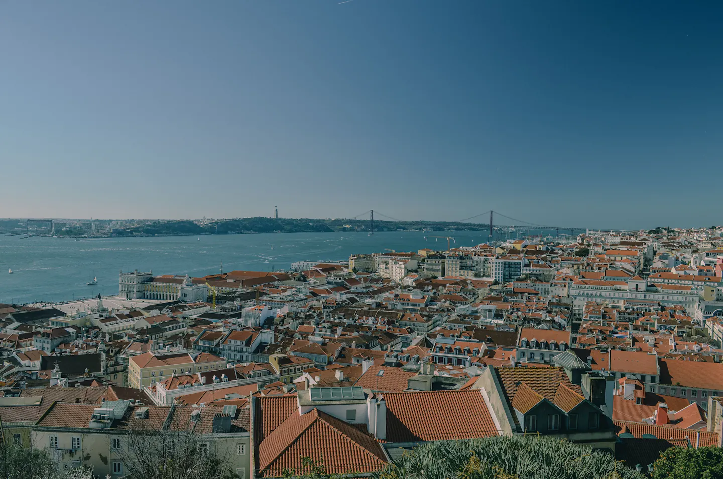 Terracotta rooftops of central Lisbon running down to the Tagus and the 25 de Abril Bridge