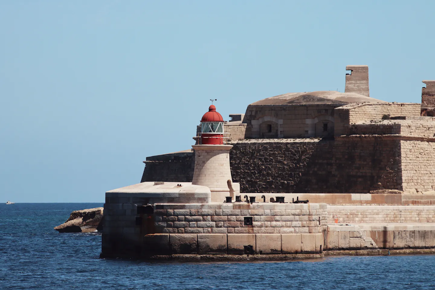The red-domed breakwater lighthouse below Valletta's stone fortifications on the Malta coast
