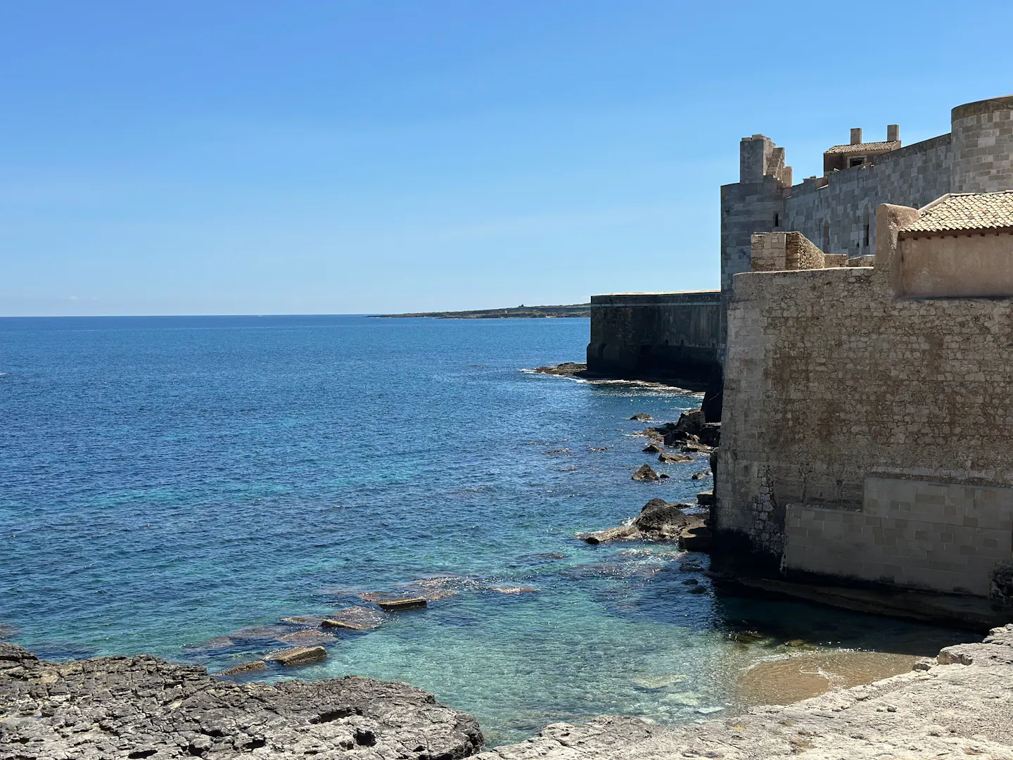 The stone sea walls of Ortigia in Syracuse above clear turquoise water on the Sicilian coast