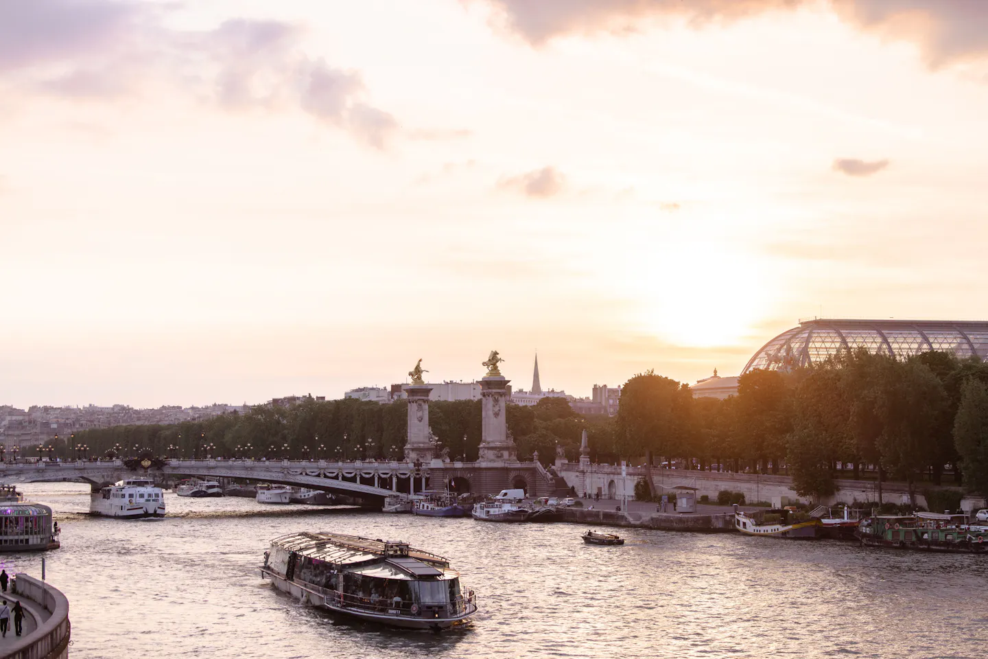 A cruise boat on the Seine at sunset passing the golden statues of Pont Alexandre III and the glass roof of the Grand Palais