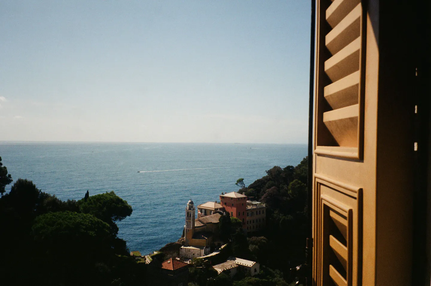 A coastal village and the open sea seen past a weathered wooden shutter
