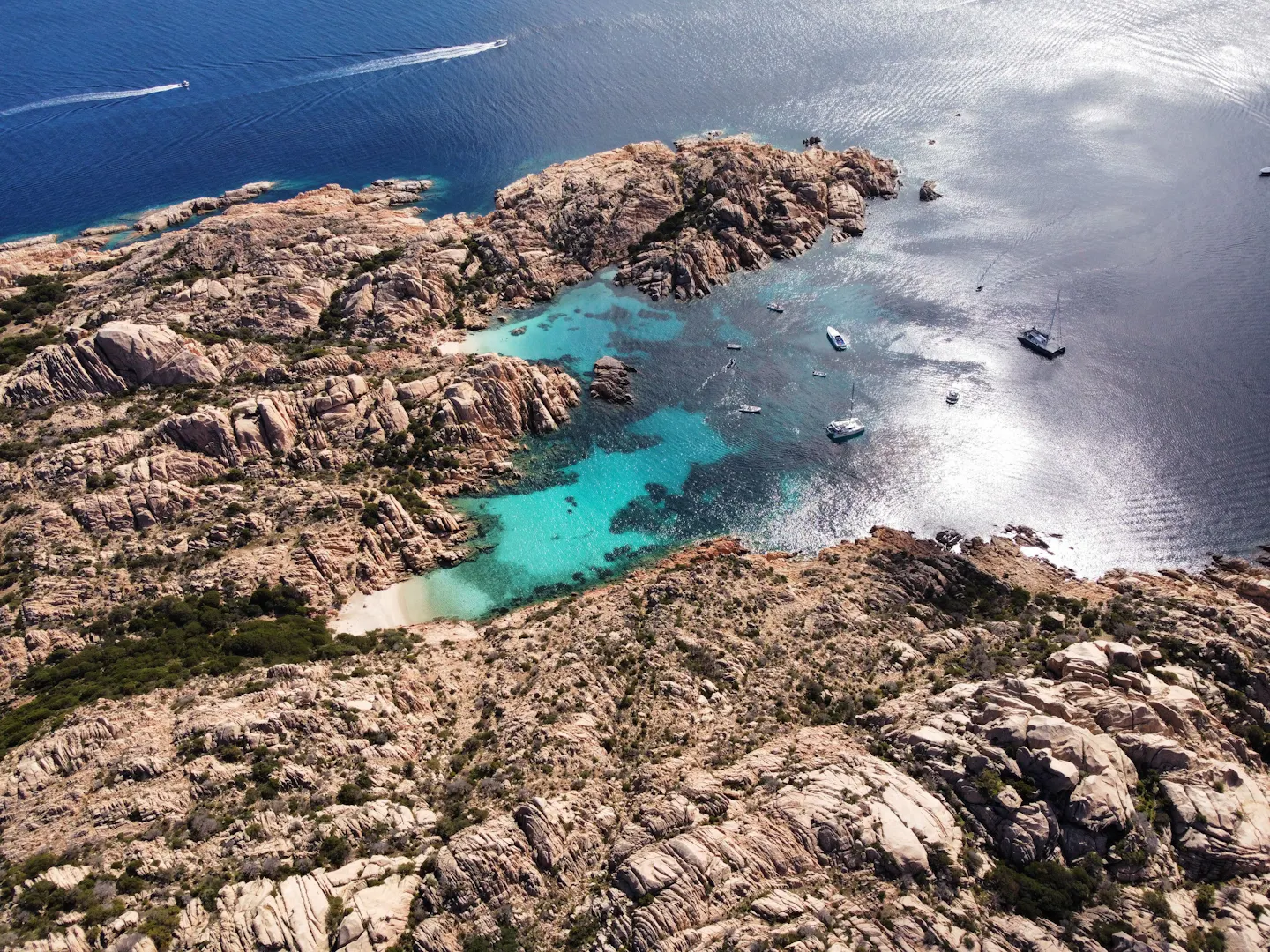 Yachts anchored off pink granite rocks above a turquoise cove in the Maddalena Archipelago, Sardinia