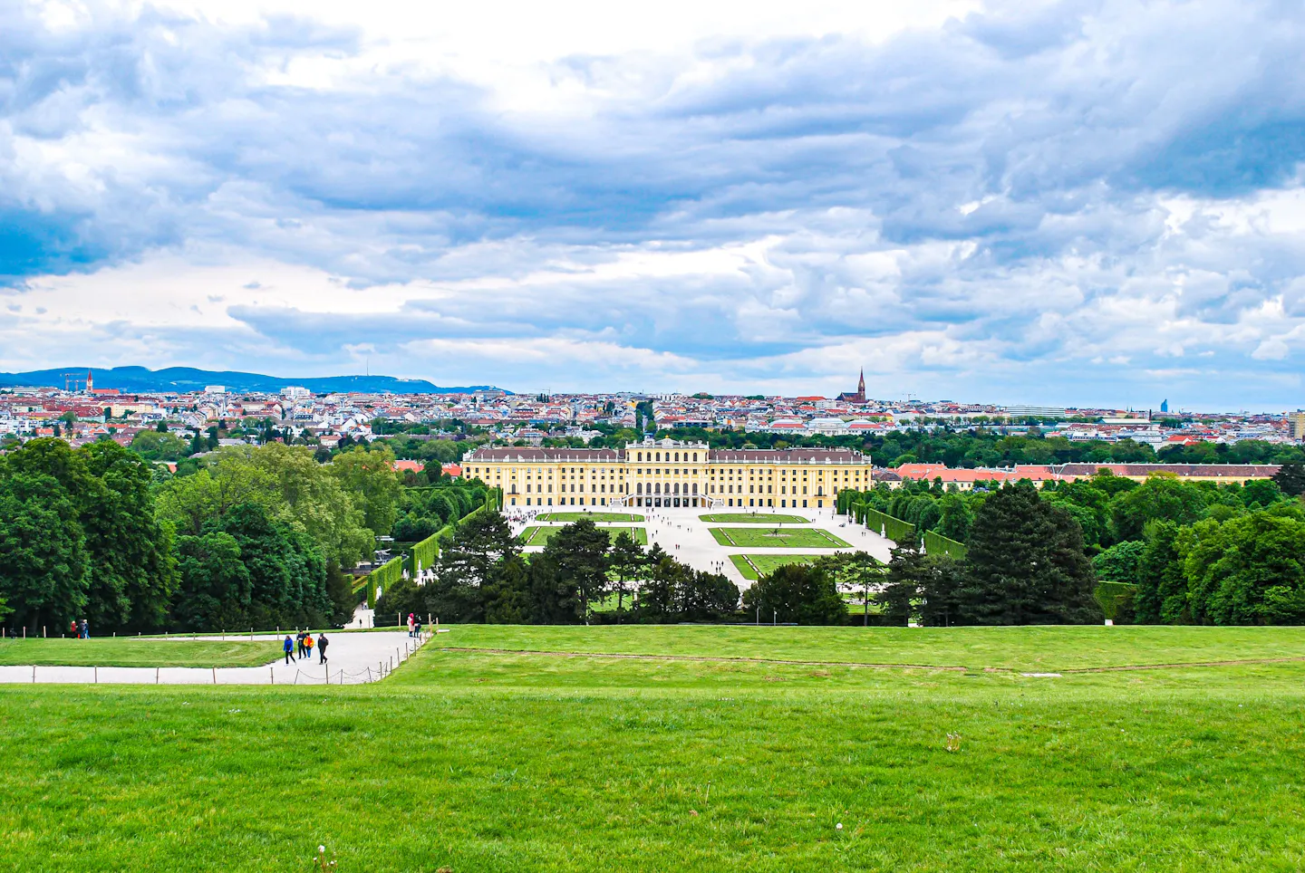Schönbrunn Palace and its formal gardens seen across a wide green meadow, with Vienna spread out behind