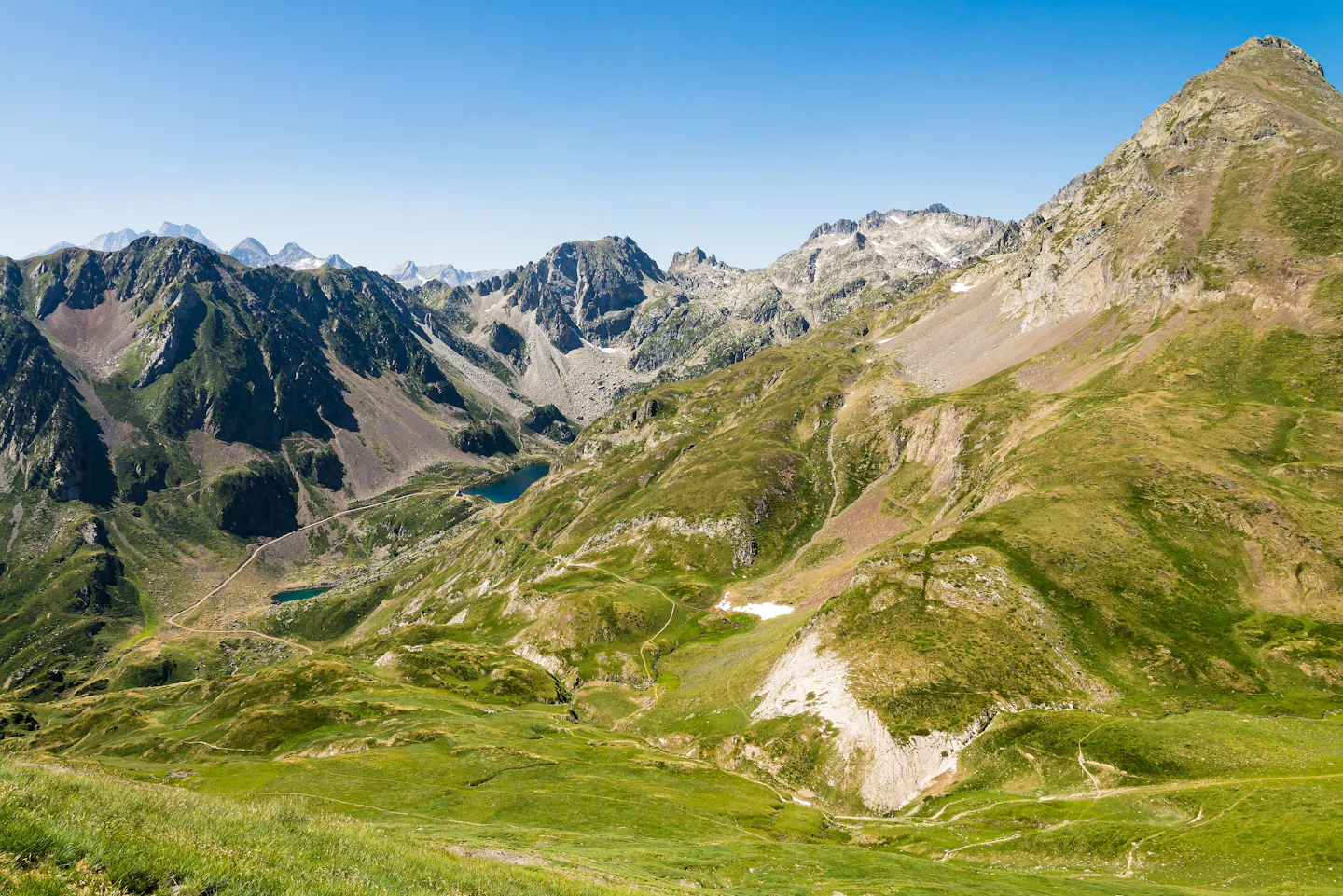 Green slopes, small blue tarns and jagged grey peaks in the French Pyrenees under a clear summer sky