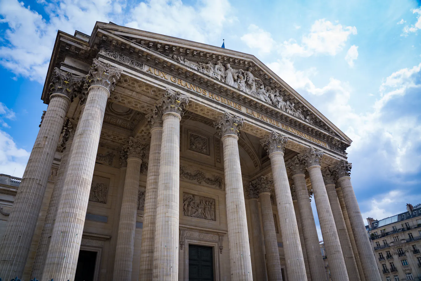 The columned neoclassical facade and sculpted pediment of the Pantheon in Paris against a blue sky