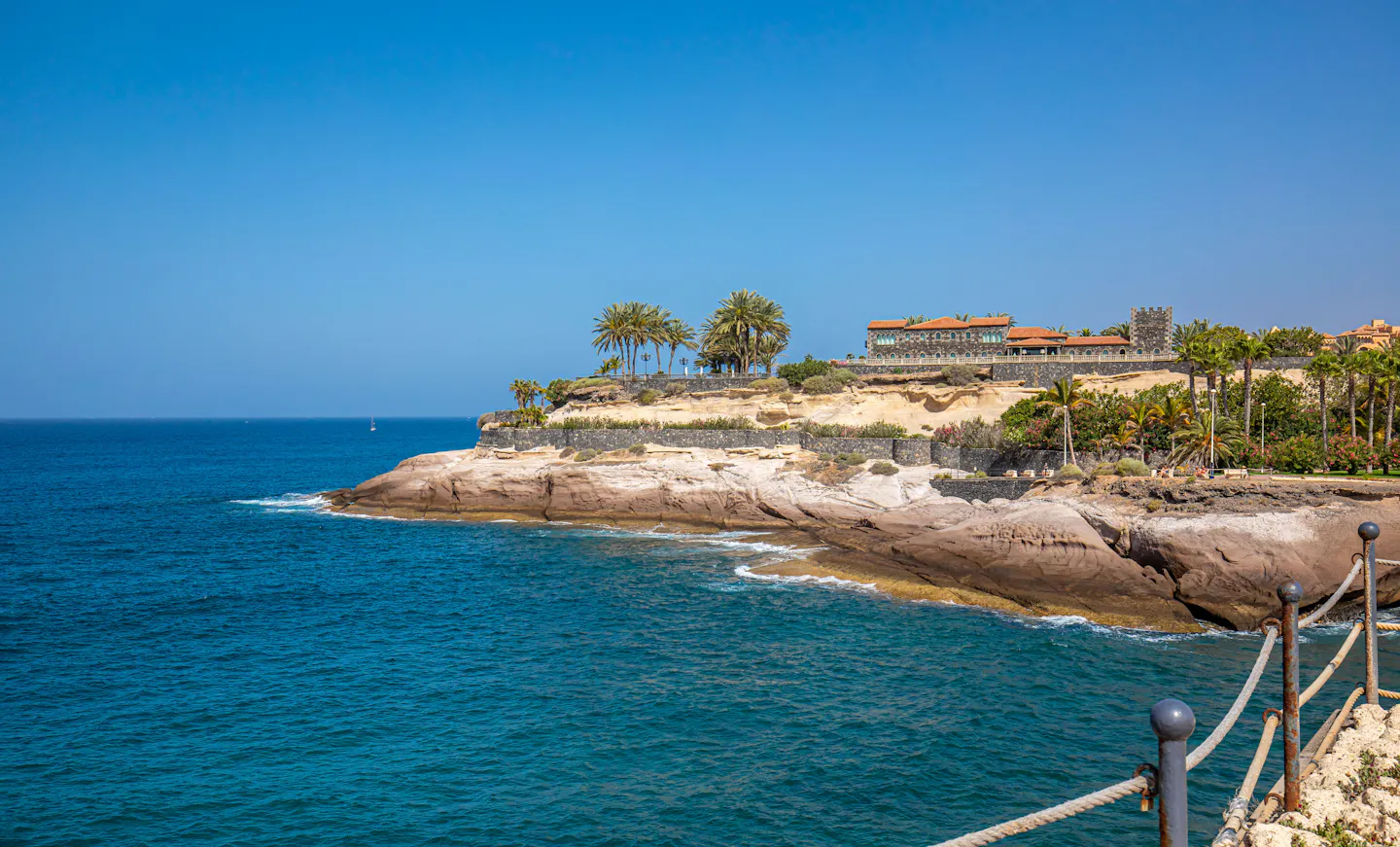 Clear blue water against low cliffs and palms on Tenerife's Costa Adeje