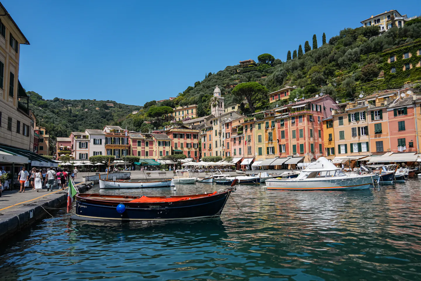 Portofino's colourful harbour lined with pastel buildings, restaurants and boats, with steep green hills behind