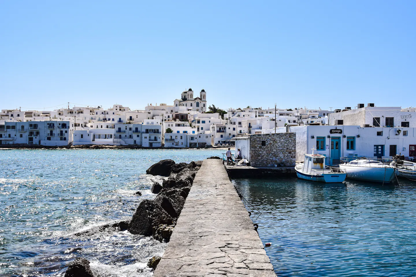 A stone jetty leading to the whitewashed harbour village of Naoussa on Paros, with fishing boats moored alongside