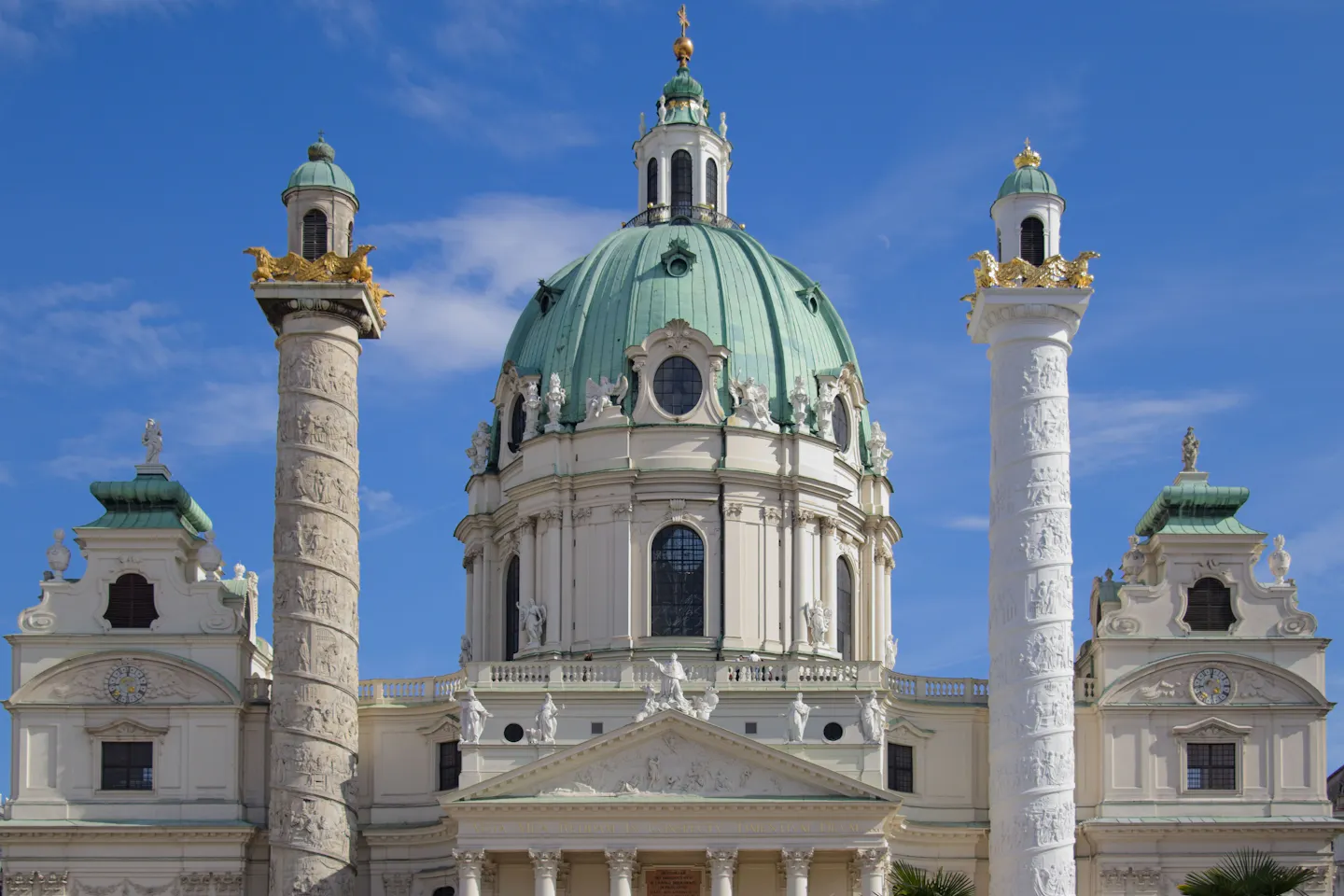 The green copper dome and carved columns of the baroque Karlskirche in Vienna against a clear blue sky