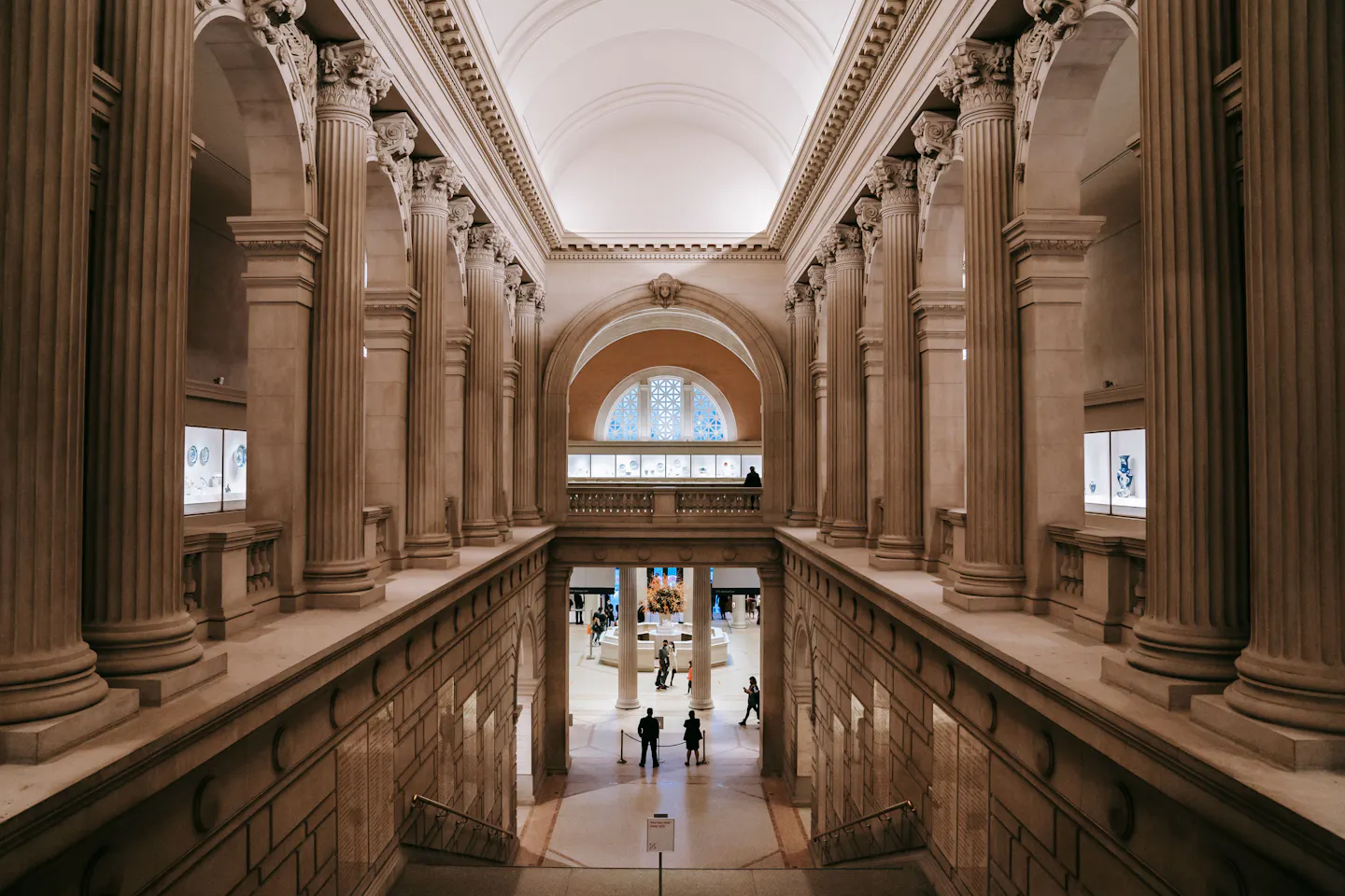 Grand columned hall and central staircase of a classical art museum, with visitors walking below