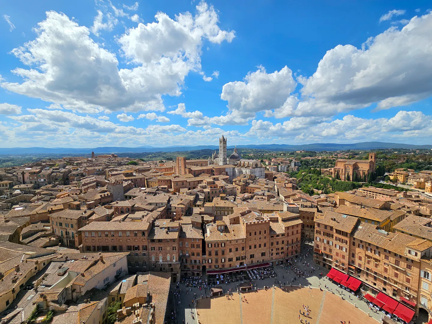 Siena's terracotta rooftops and the shell-shaped Piazza del Campo under a big cloud-streaked sky